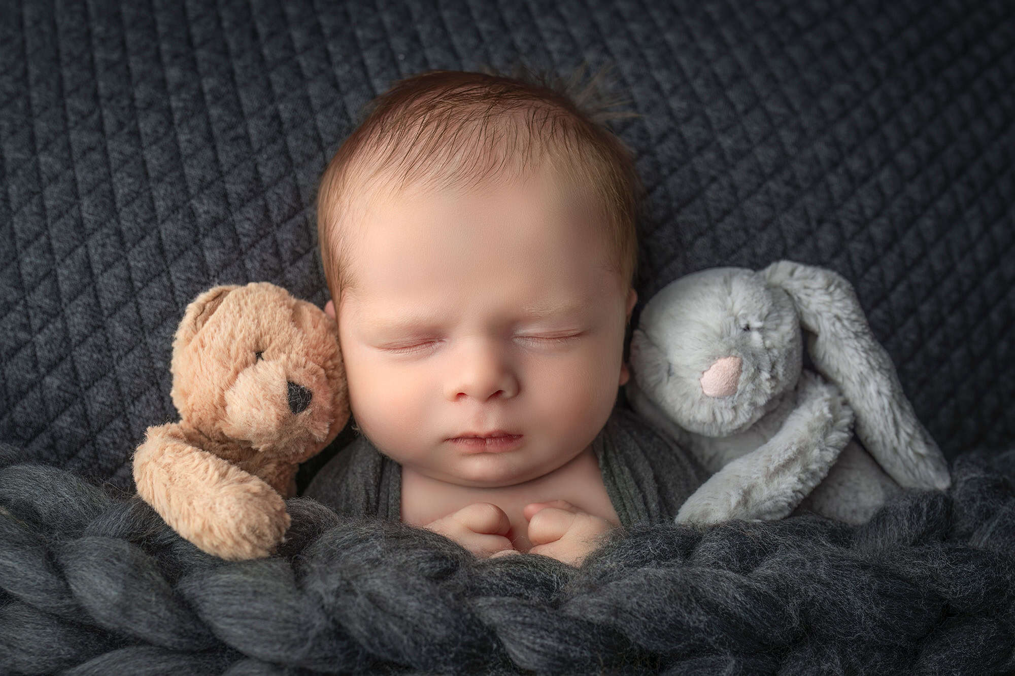 Newborn boy asleep snuggled in between a stuffed bear and bunny