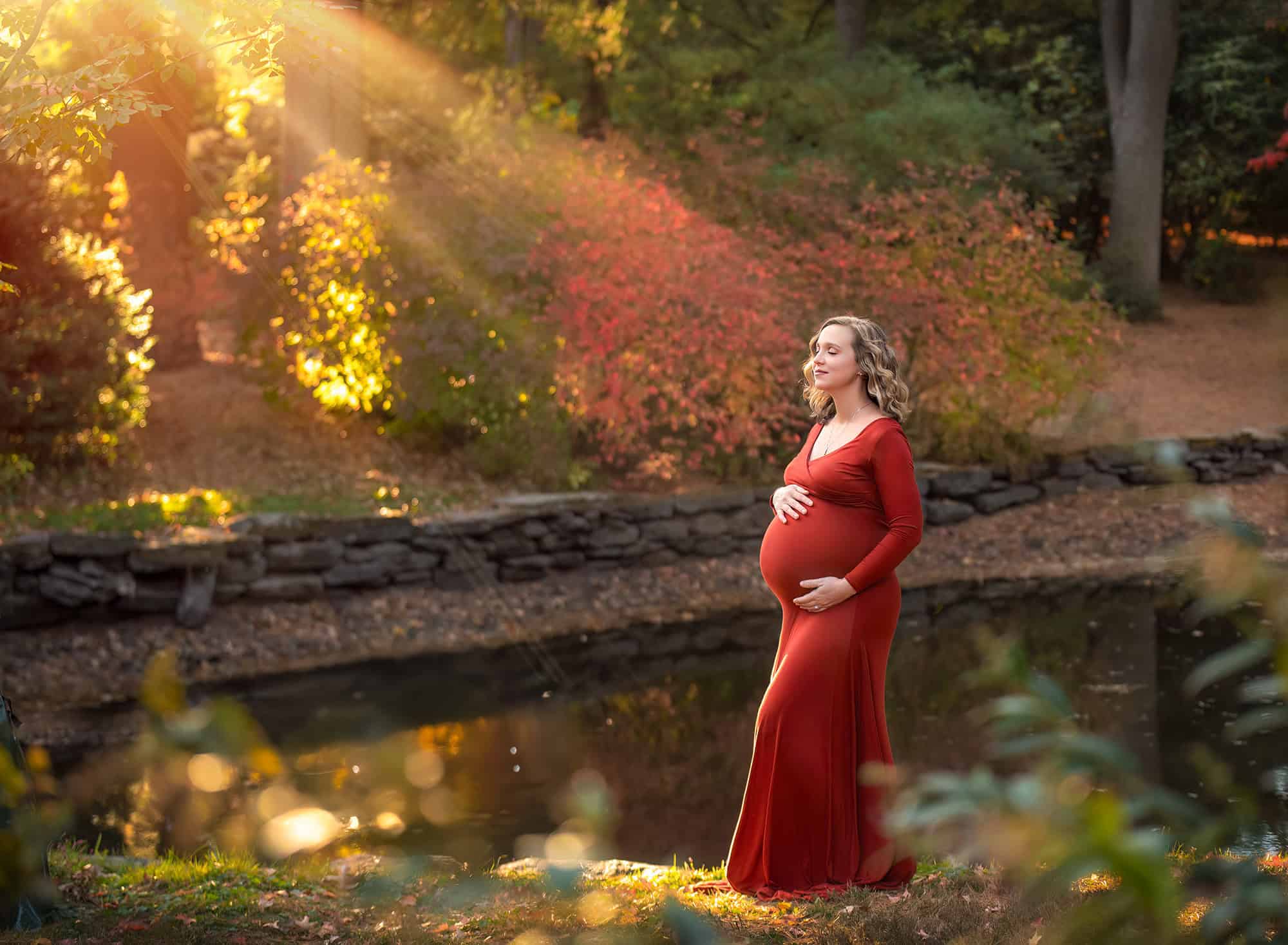 maternity and newborn photography pregnant woman feeling the sun shine down on her face and belly in autumn