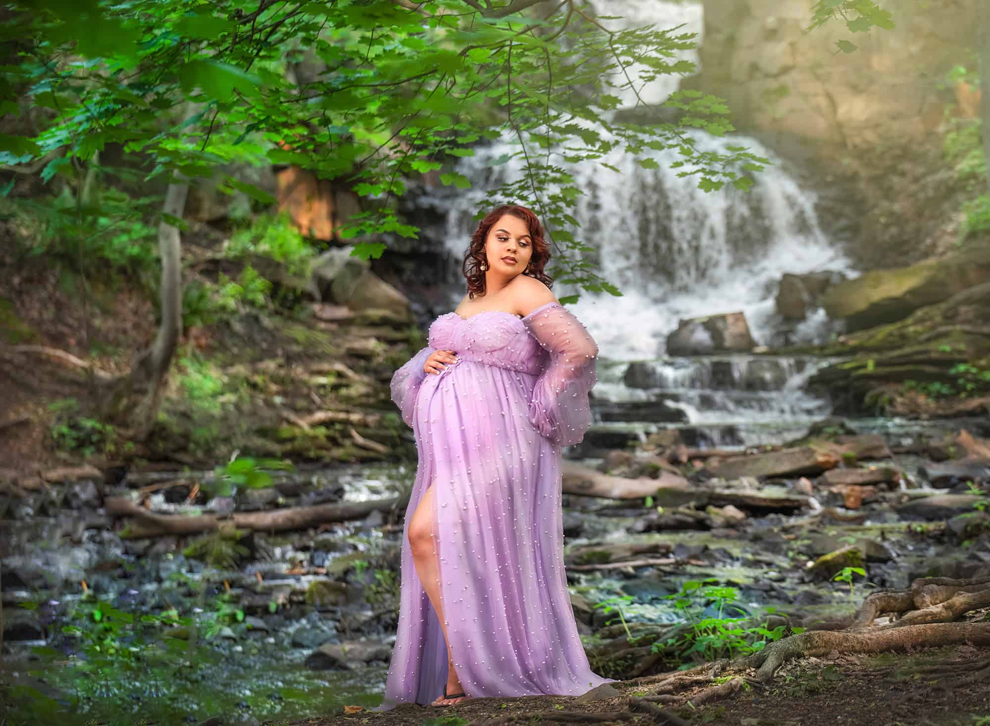 maternity and newborn photography pregnant woman posing in light purple dress in front of a waterfall in summer