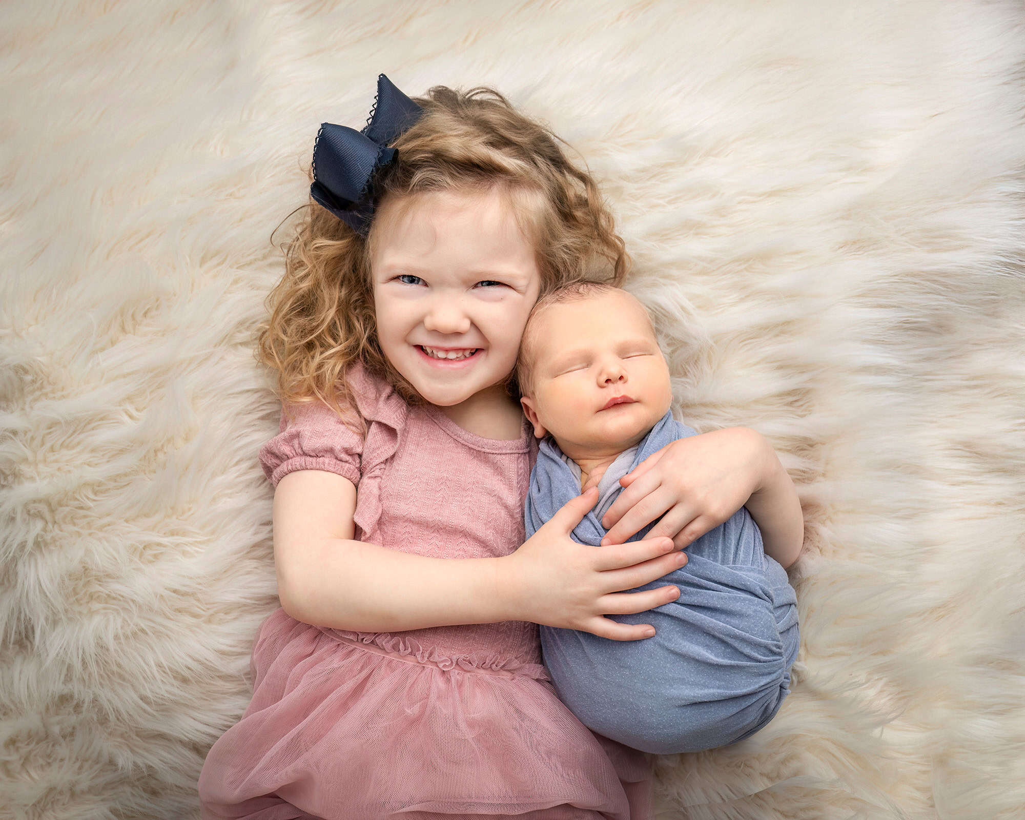 Big sister Cece lying beside newborn Tommy with her arm around him