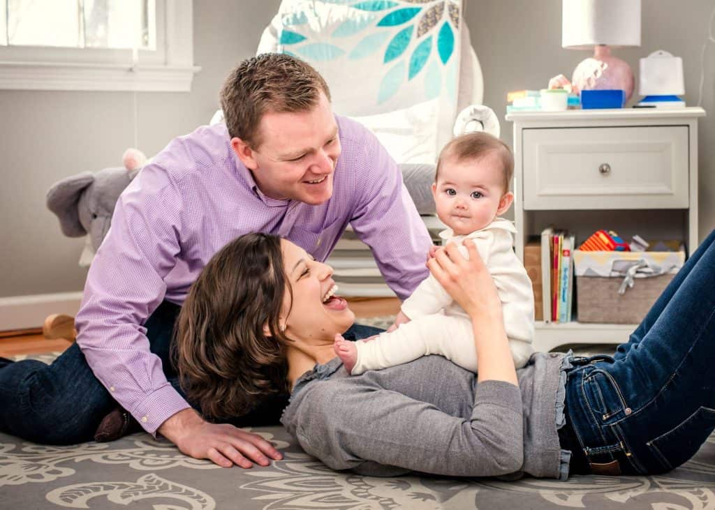 6 month old baby playing with her parents in her nursery