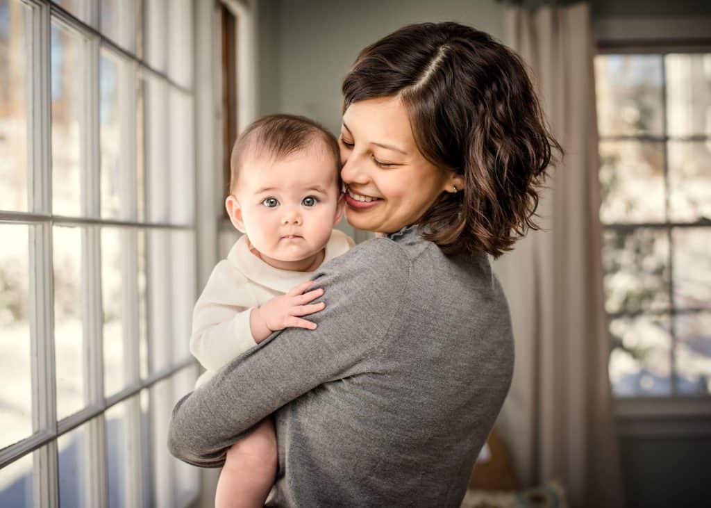 Mother holding her 6 month old baby over her shoulder smiling down on her