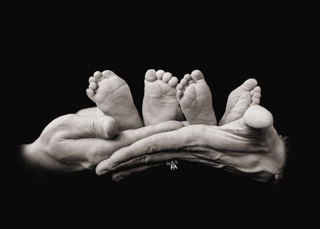 mom and dad's hands holding 2 babies feet black & white