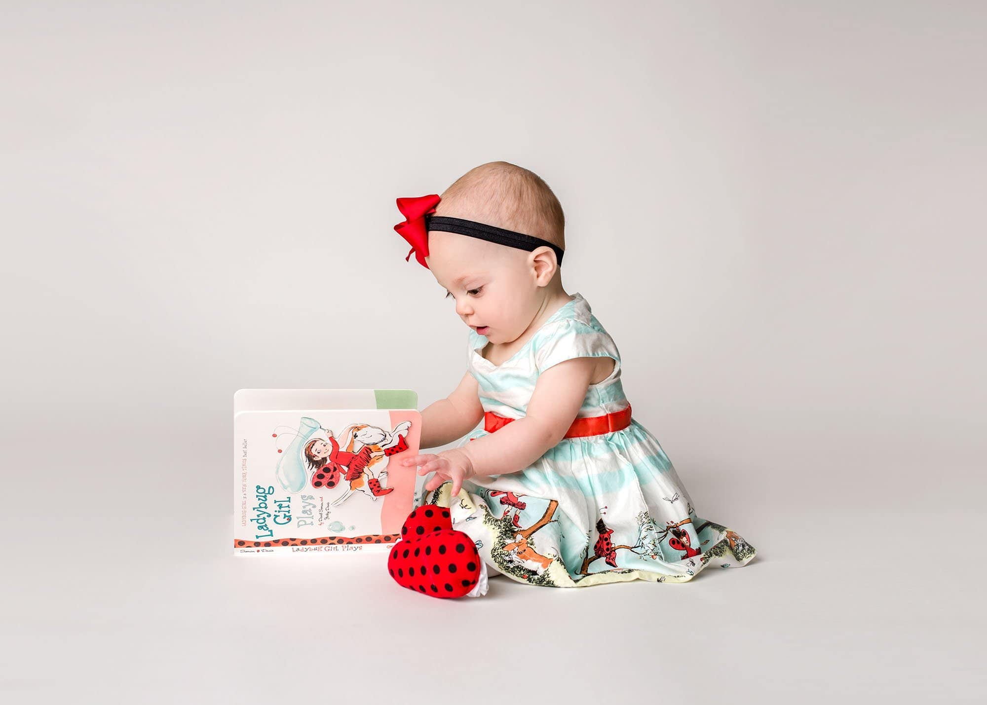 one year old baby girl reading "Ladybug Girl" in ladybug girl dress Glastonbury CT Baby Photographer One Big Happy Photo www.onebighappyphoto.com/babies