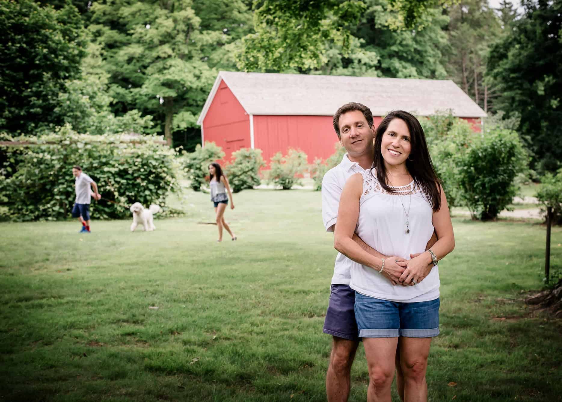 Mom and Dad pose while kids and dog play in the background