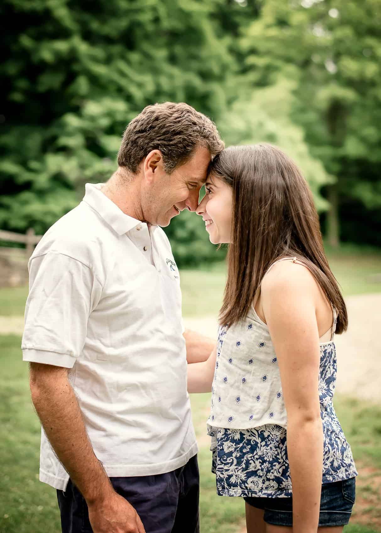Dad and teen daughter rest forehead to forehead in smiles outside in summer