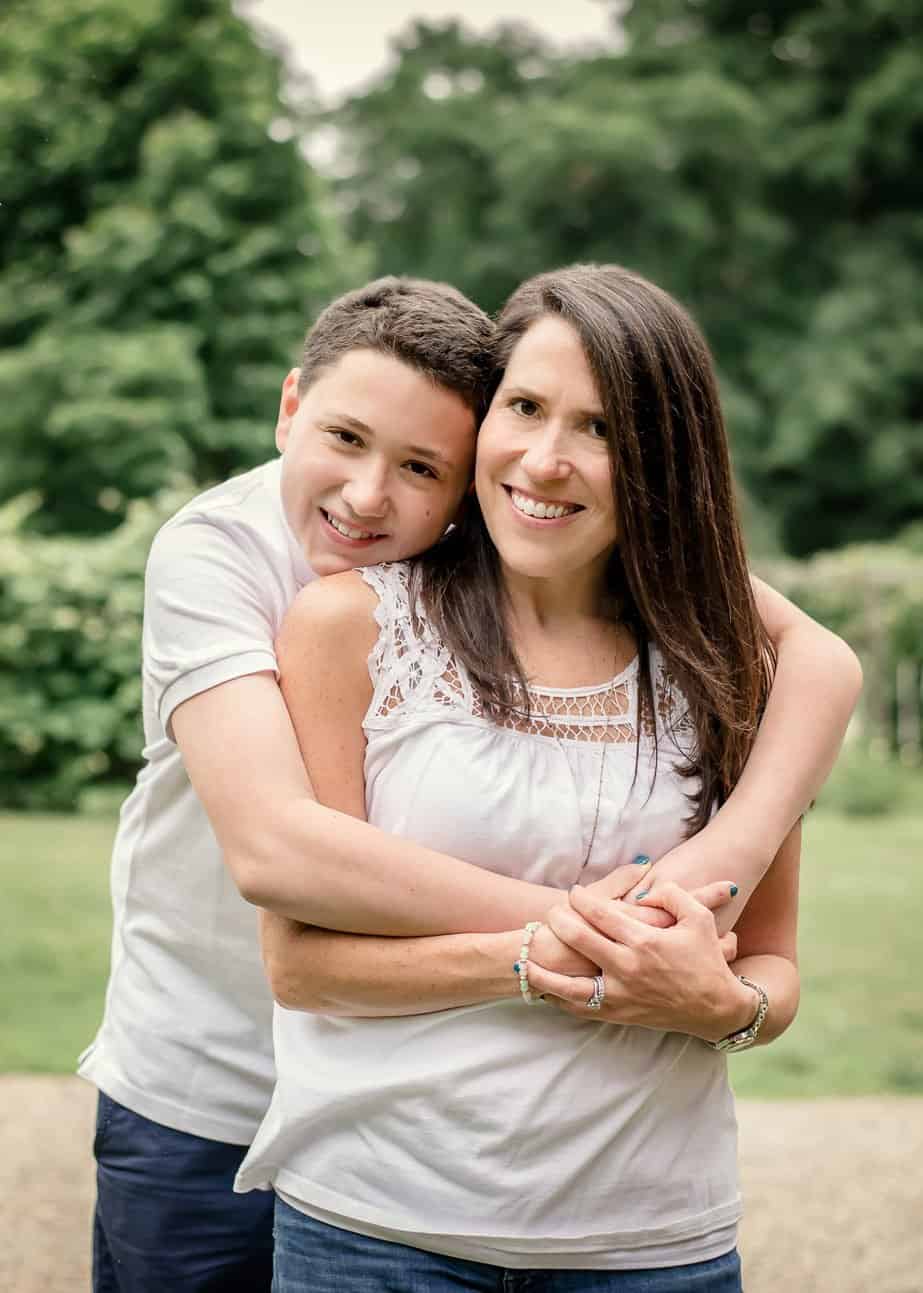 young son hugging his Mom from behind her outside in summer
