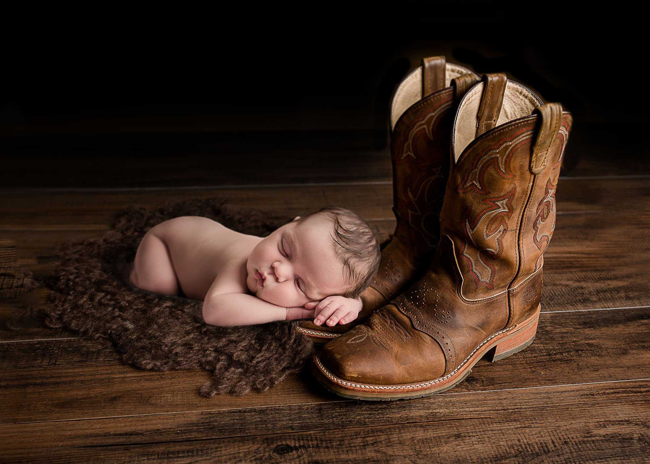 Newborn baby sleeping with head and hands on cowboy boots One Big Happy Photo Amber Sehrt