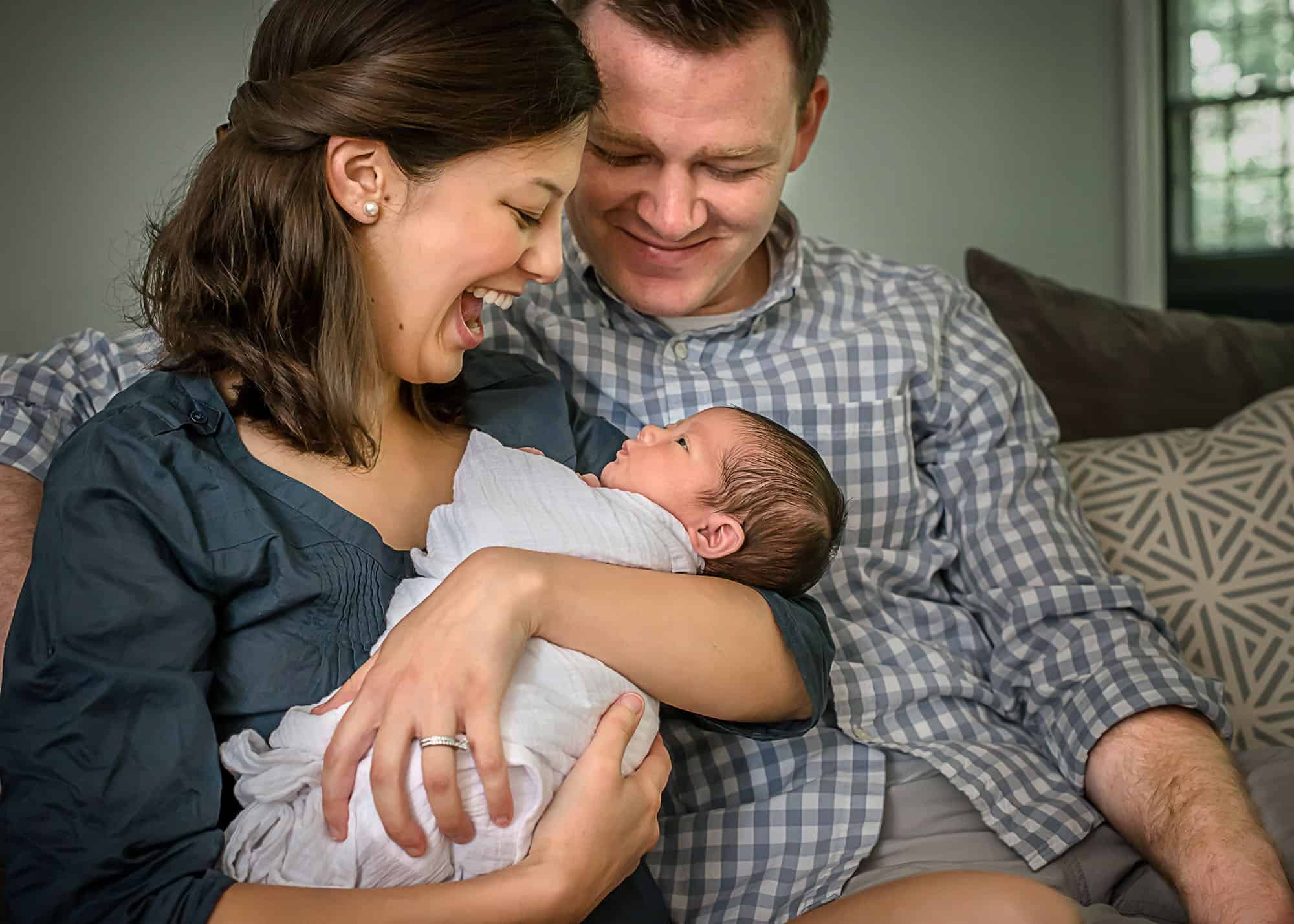 Momma holding newborn baby girl while Daddy smiles down at the baby