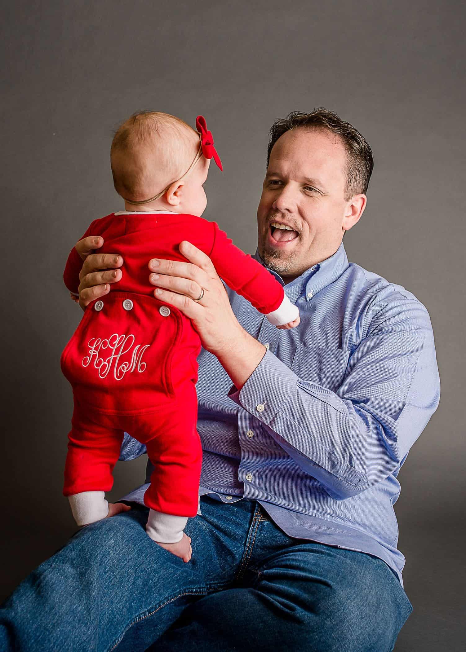 Daddy holdings standing 6 mo old baby girl in red long pajamas One Big Happy Photo