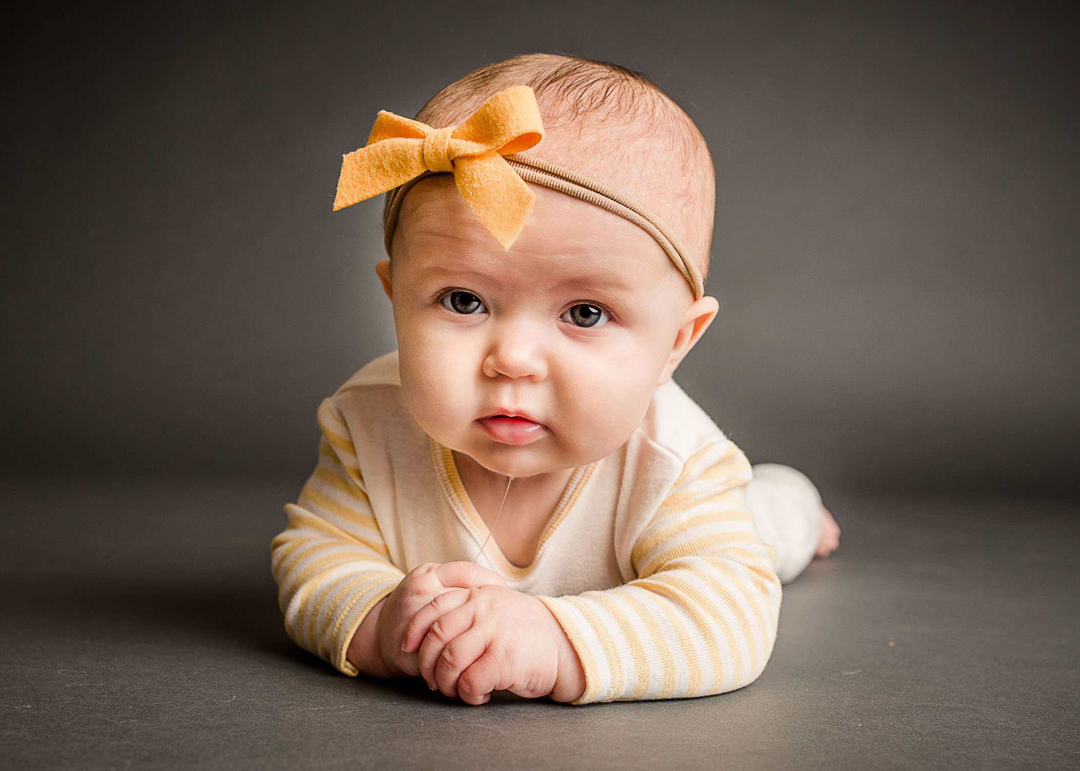 Baby girl with yellow bow holding her hands while a string of drool falls from her chin One Big Happy Photo