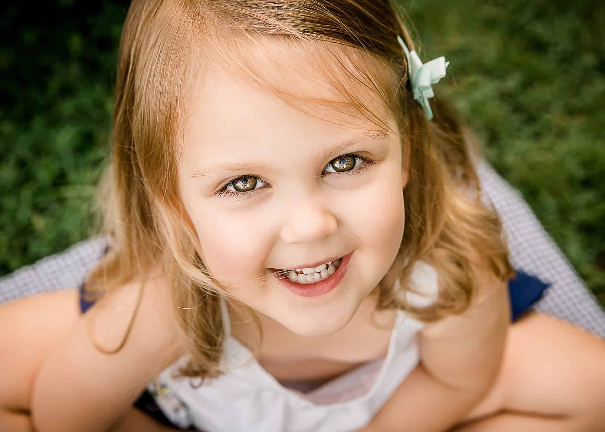 blonde 3 year old girl looking up outside with the reflection of clouds in her eyes