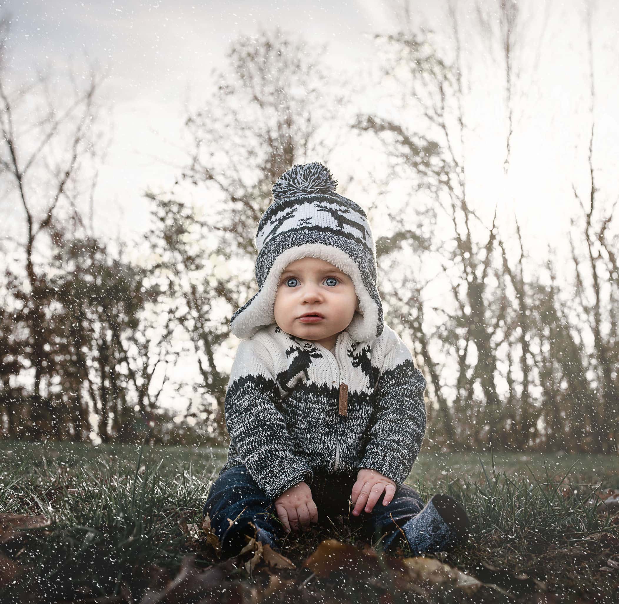 6 month old baby boy sitting outside as snow begins to fall