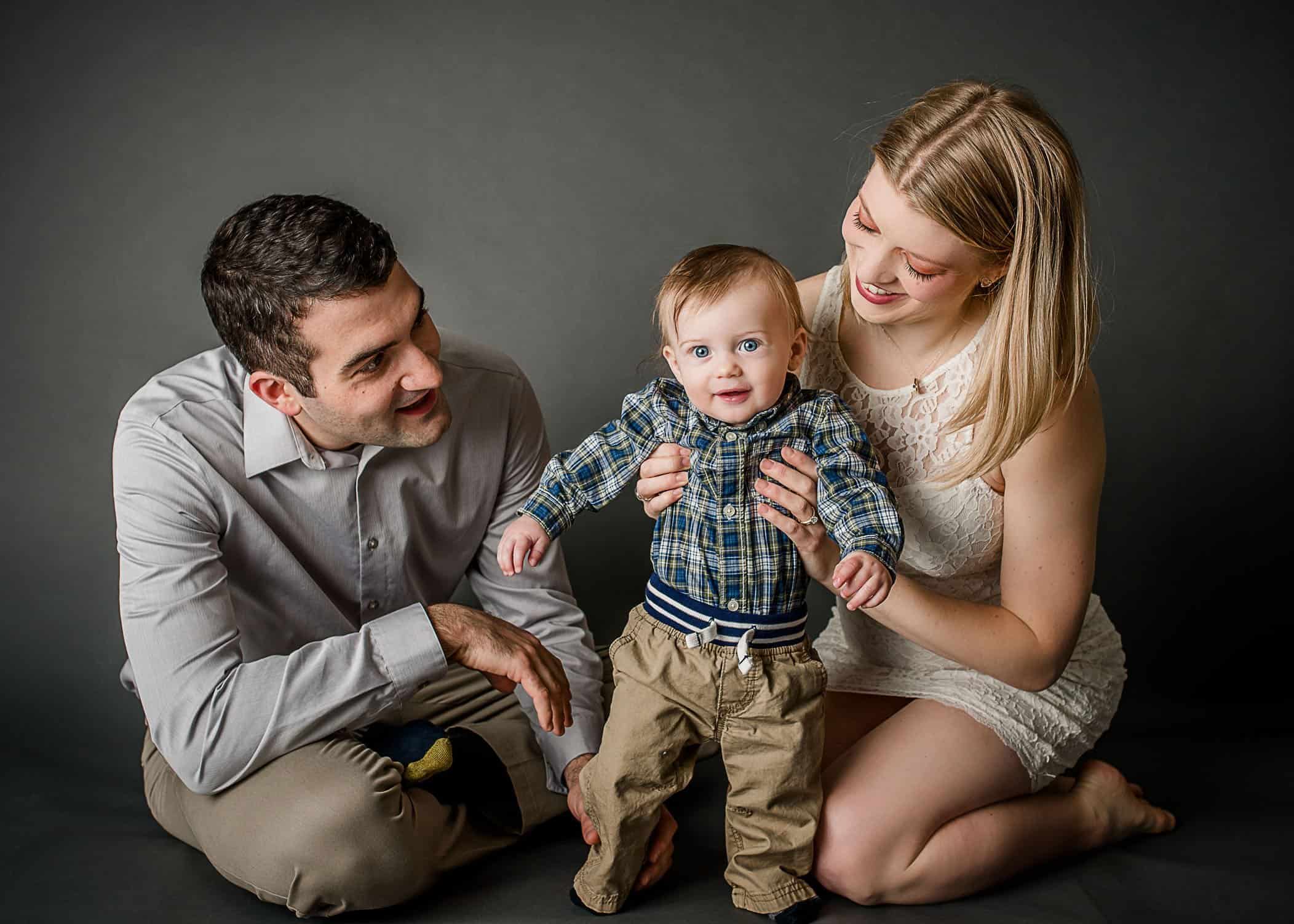 6 month old baby boy standing up with Mom and Dad's help