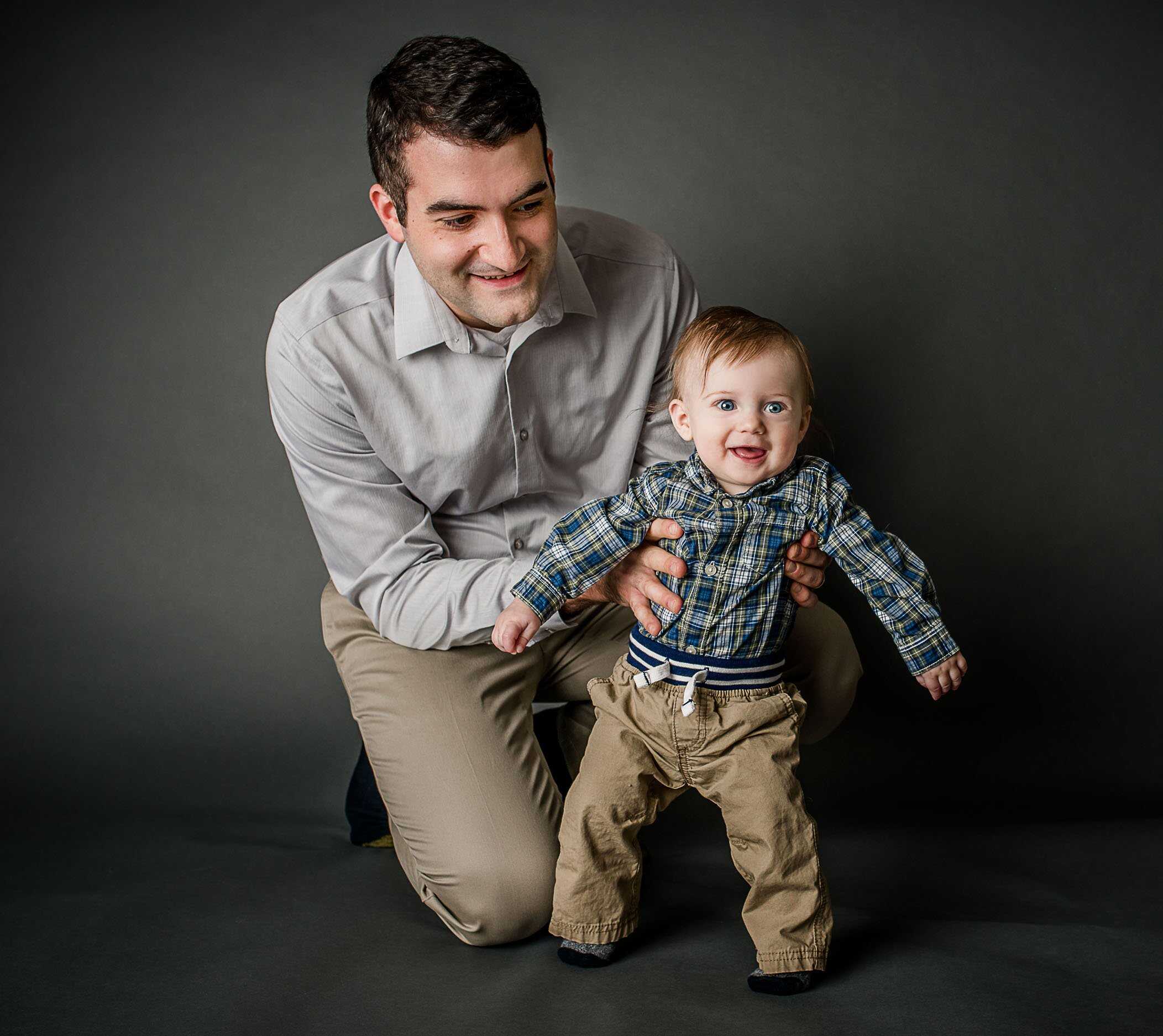 6 month old baby boy standing up with Dad holding his waist