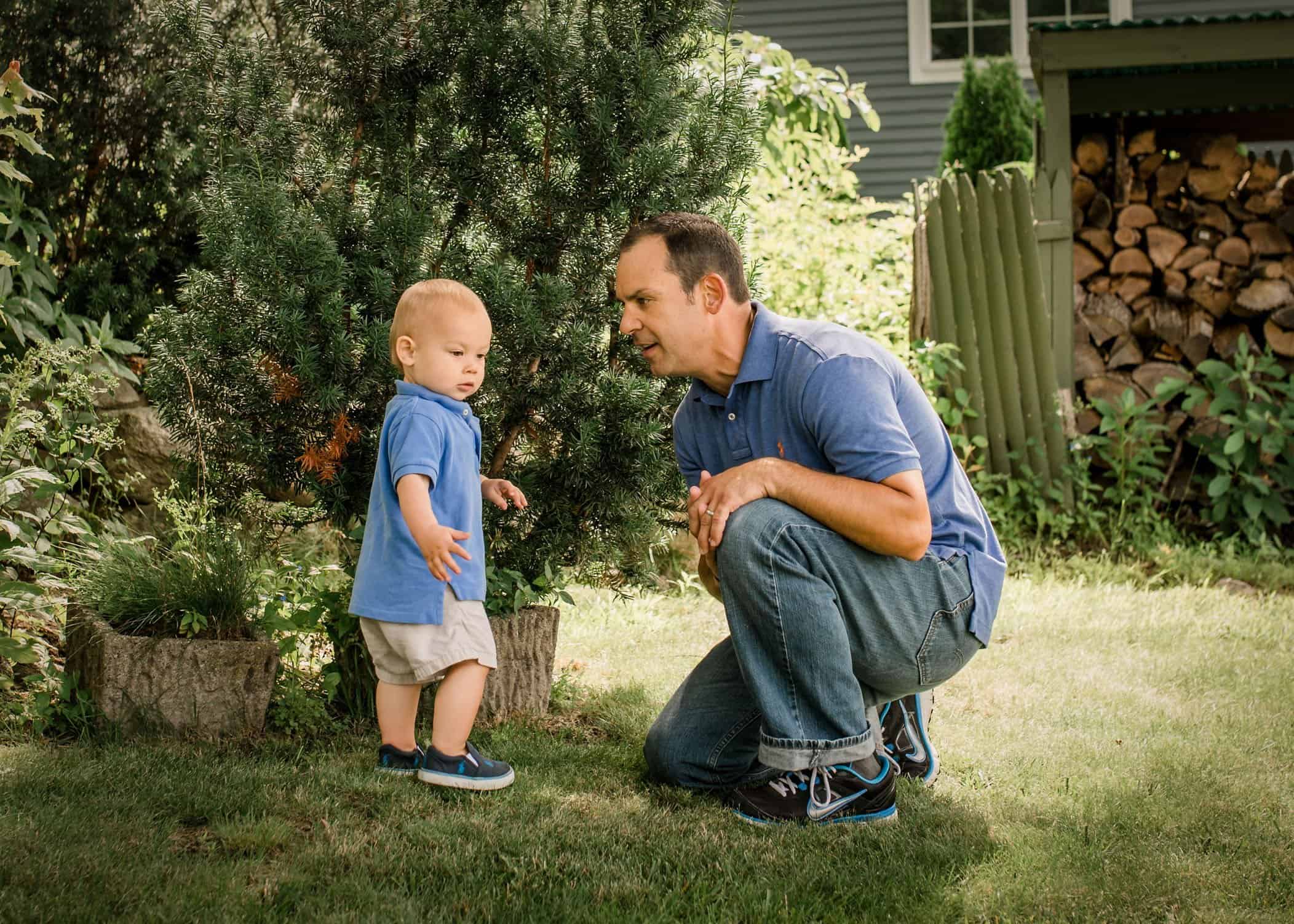 Dad trying to catch the attention of his one year old son outside in the garden