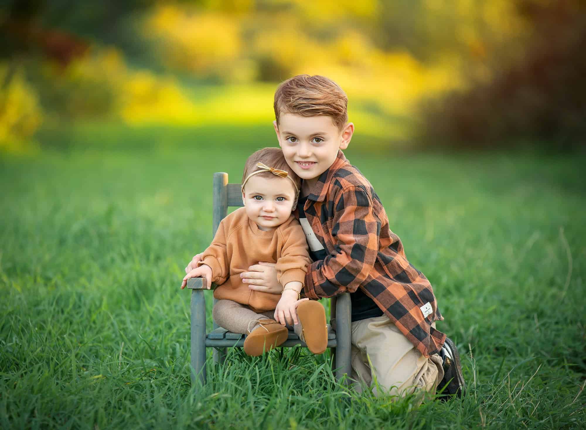 Outdoor family photoshoot in Glastonbury CT toddler girl sitting in nature with big brother sitting next to her