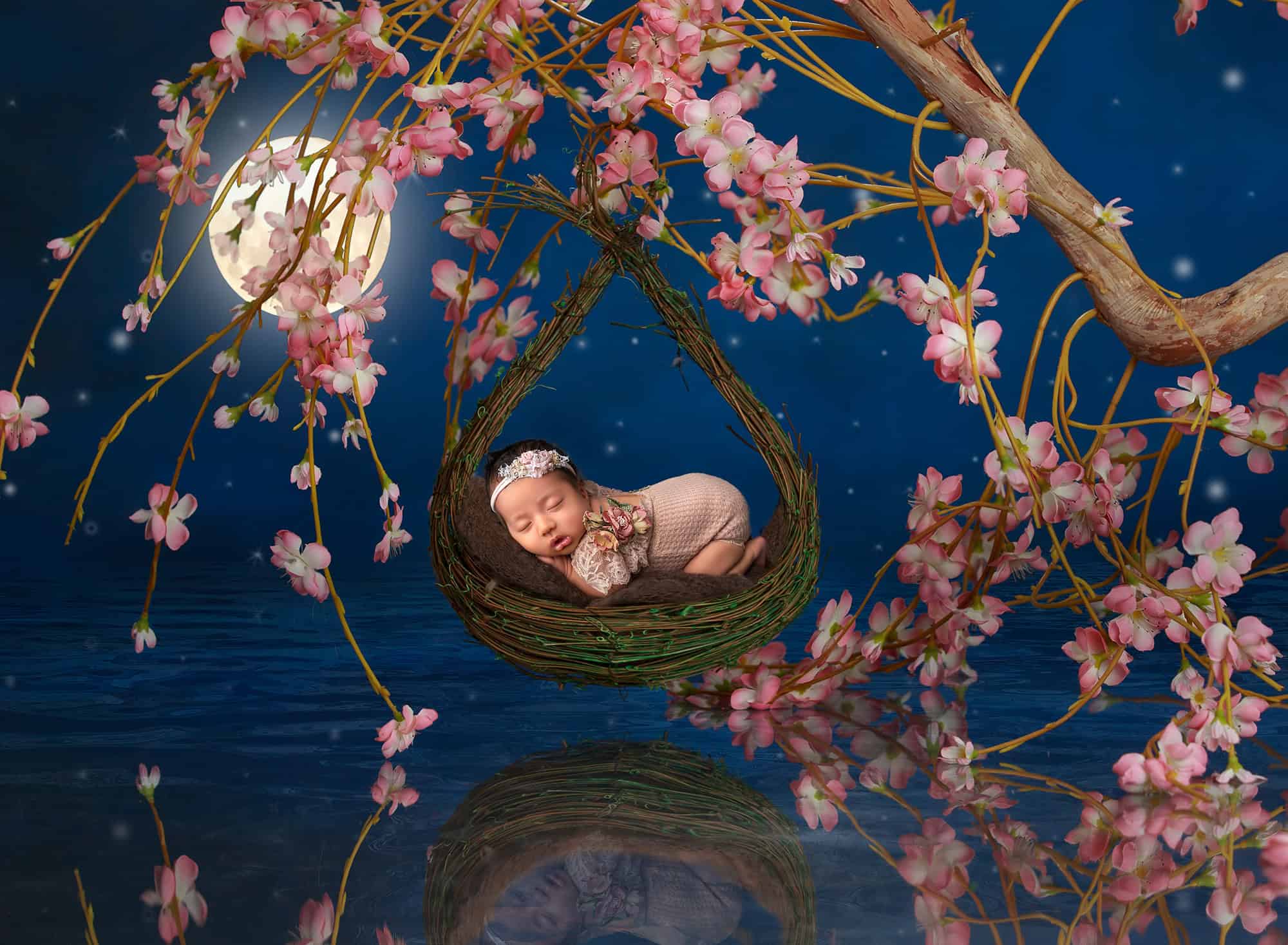 posed newborn photography session baby sophie sleeping on a swing under the moonlight and cherry blossoms.