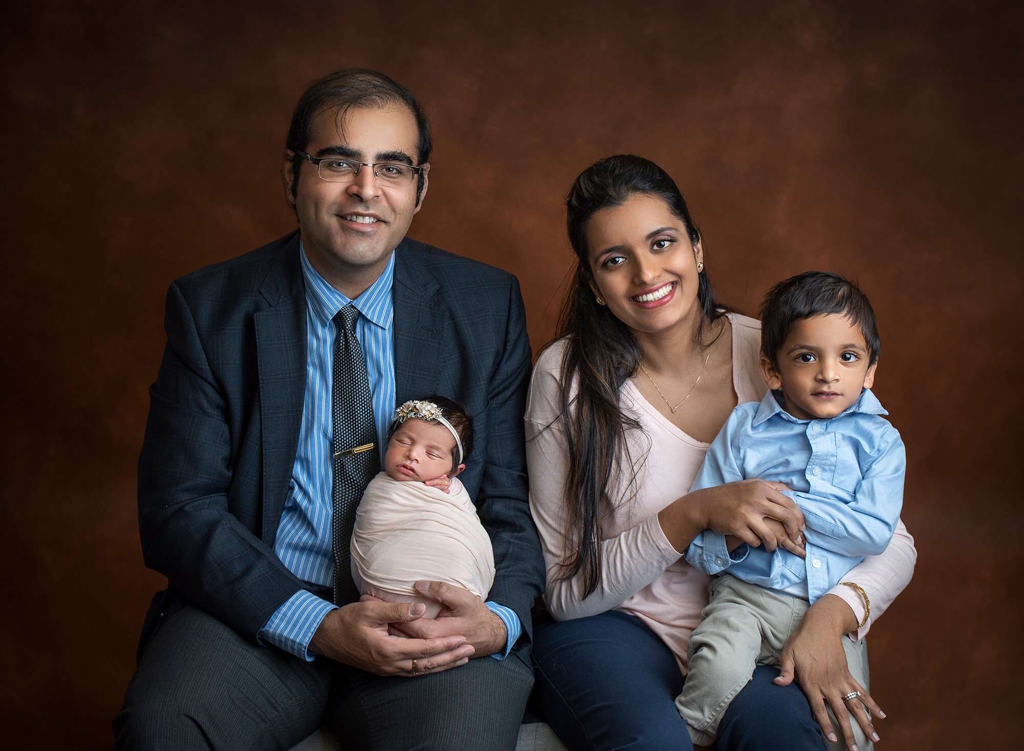 Professional Maternity Newborn Photographer mother and father sitting with son and newborn baby girl on amber background