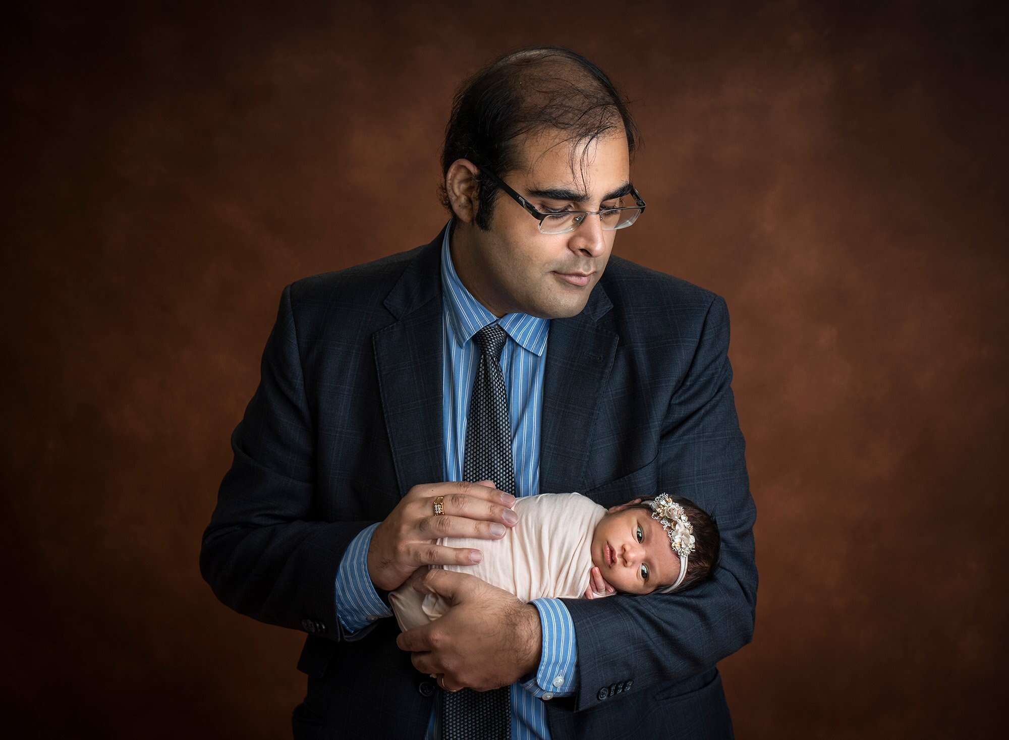 new dad cradling newborn baby girl swaddled in ivory