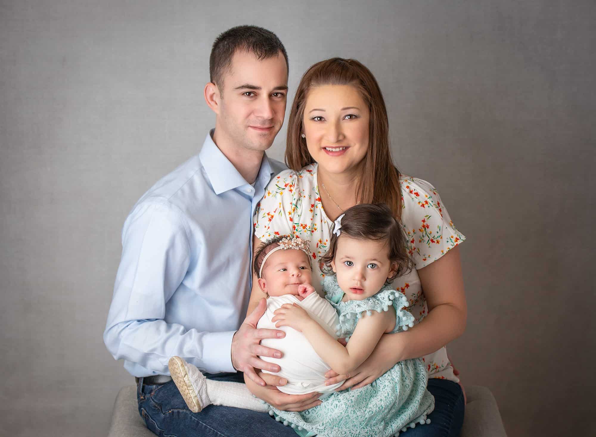 smiling couple on gray backdrop holding daughters