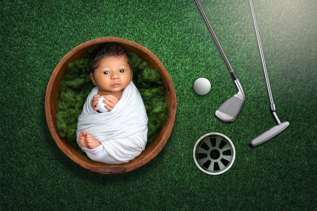 Awake newborn in round bowl with golf props during themed portrait