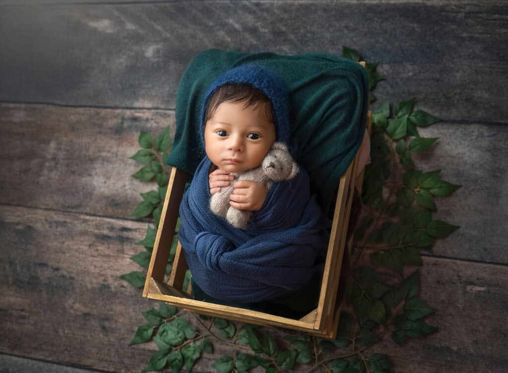Awake newborn wrapped in navy and teal tones in wooden crate portrait