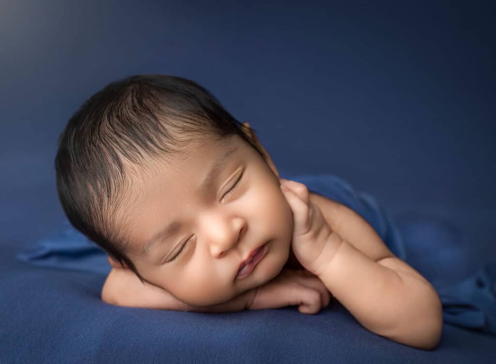 newborn and family photography pose with baby resting on forearms on deep blue fabric