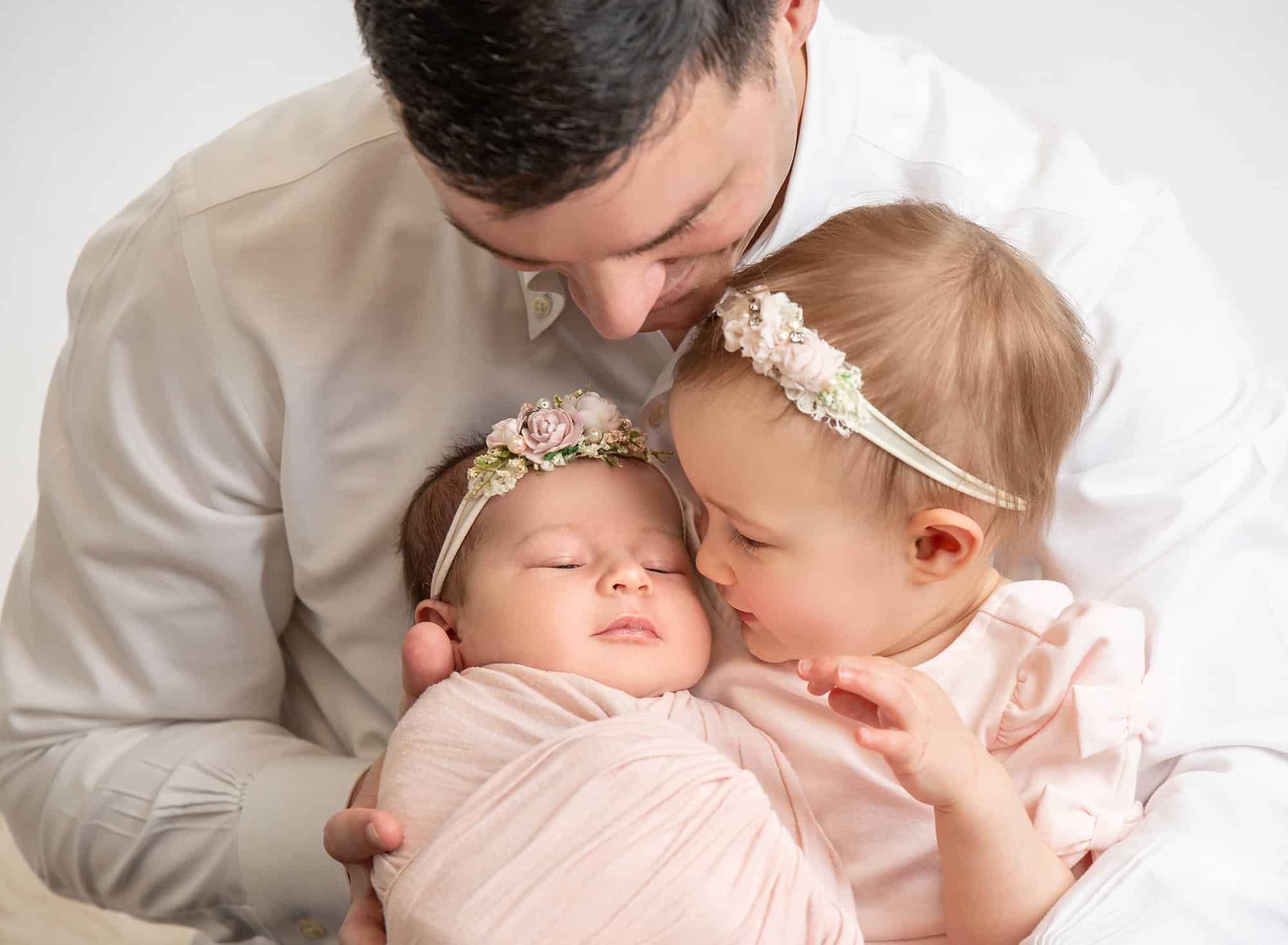 dad looking down at his two beautiful baby girls in soft pink