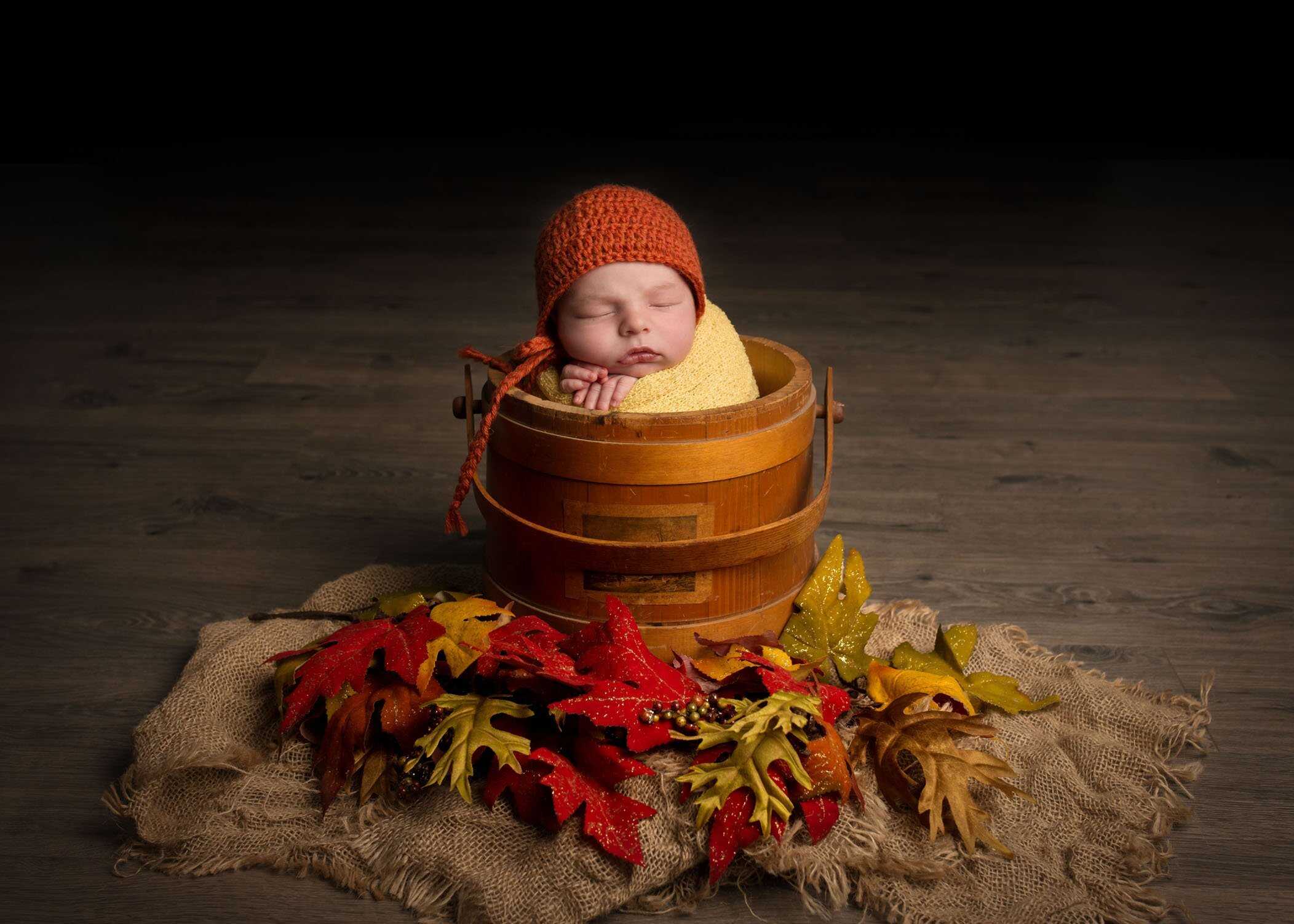 sleeping newborn in sugar bucket with fall leaves and colors