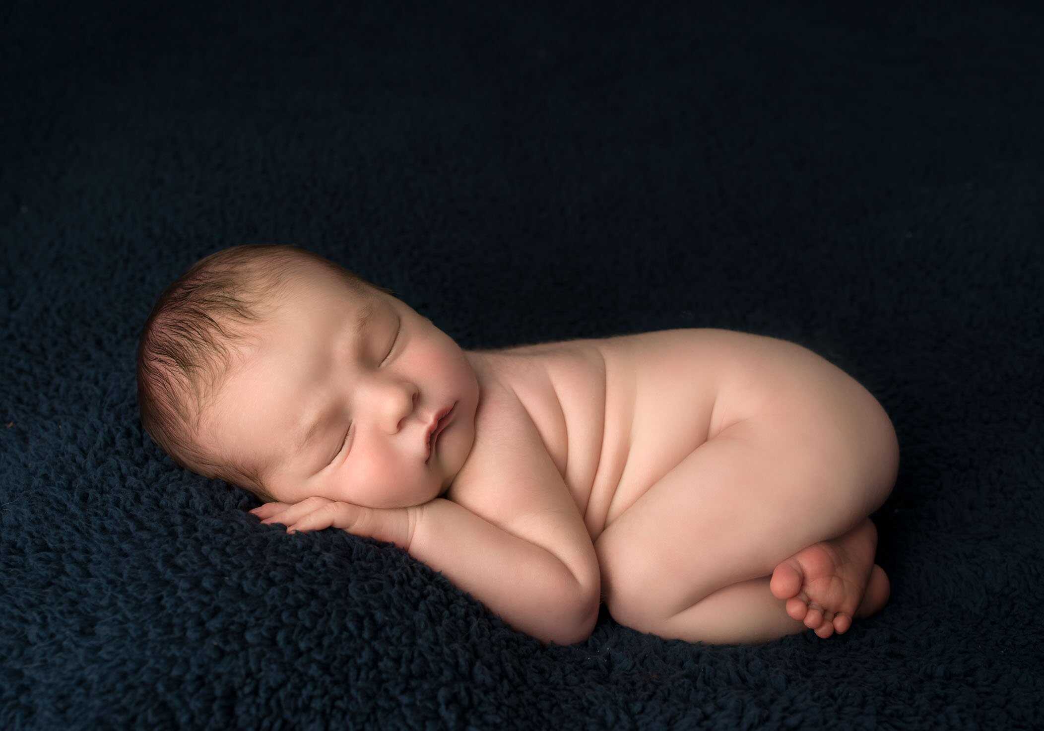 newborn boy sleeping in bum up position on navy