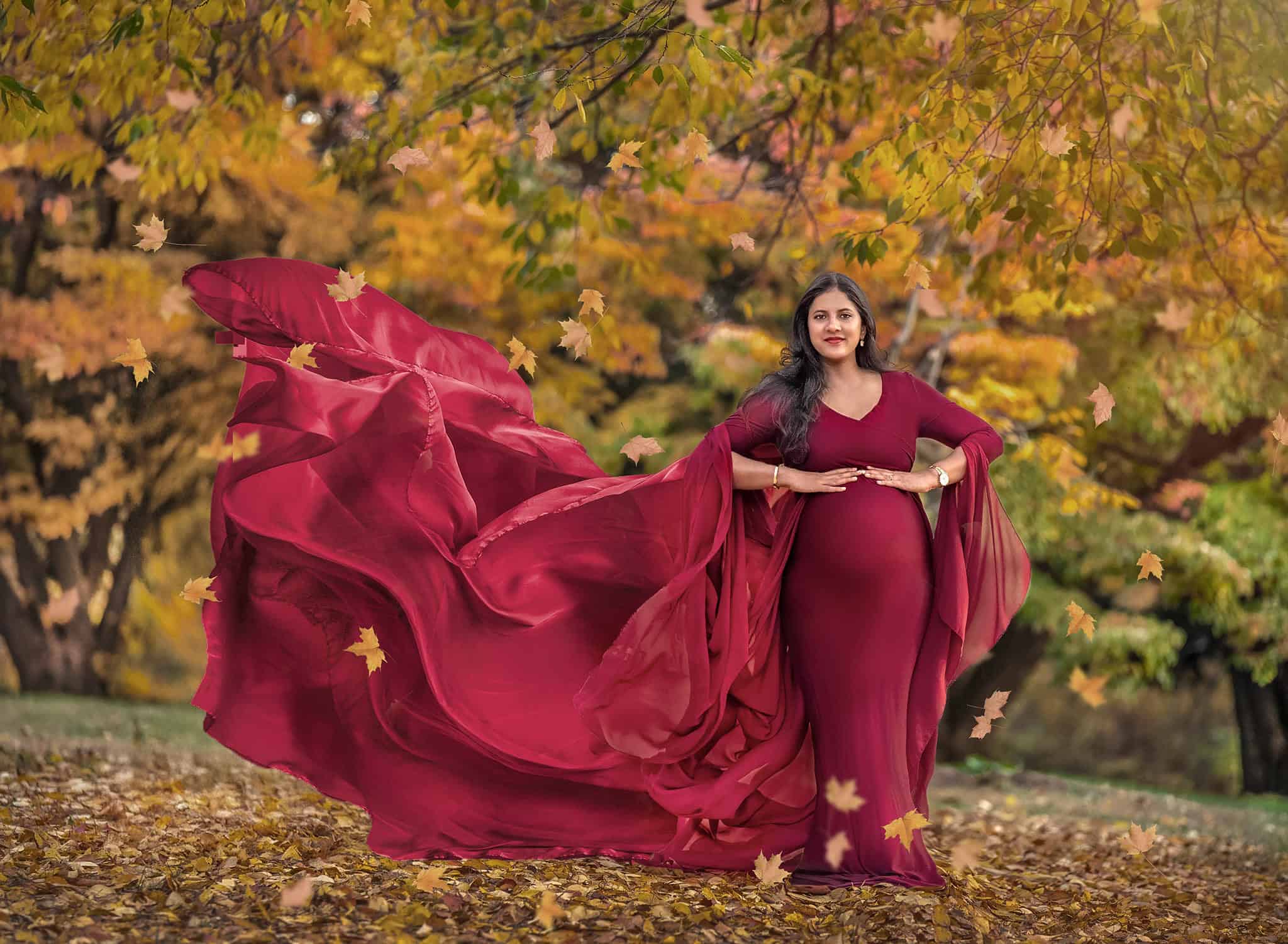 Fine art maternity photography Pregnant woman in flowing cranberry gown standing in autumn landscape