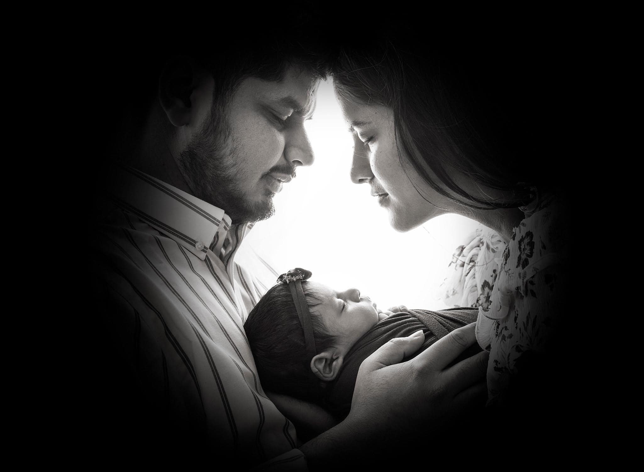 Parents touching foreheads while embracing newborn baby in a black and white photo