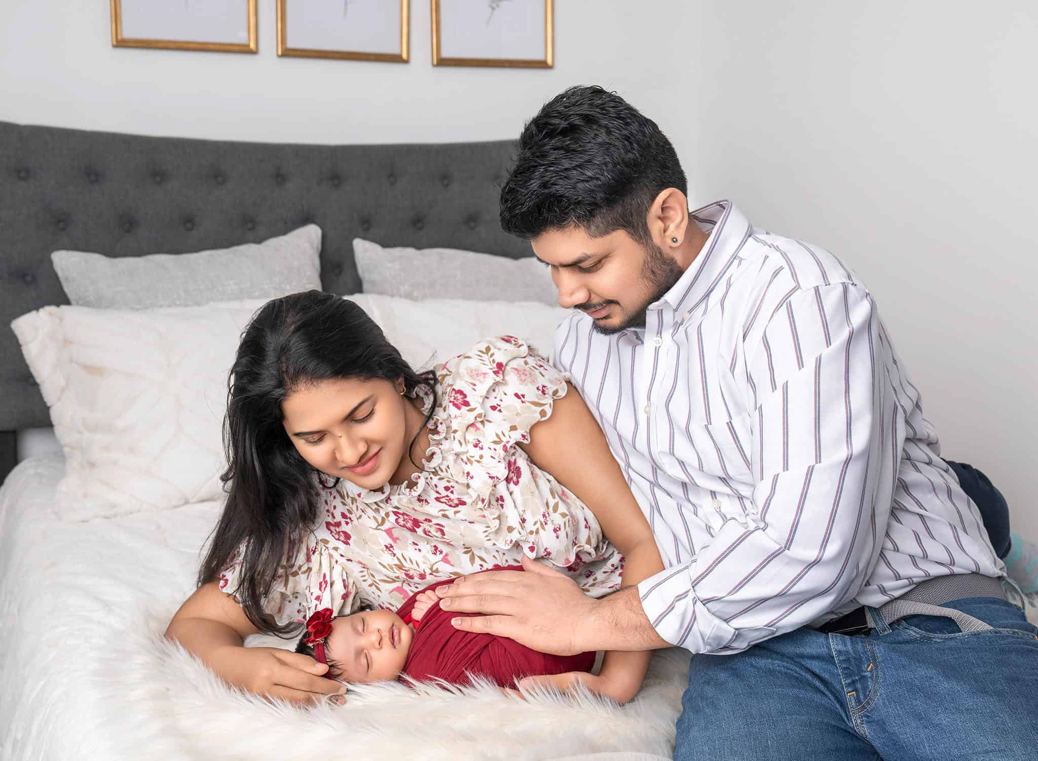 Parents holding baby Dhanya laying on bed with joyful expressions