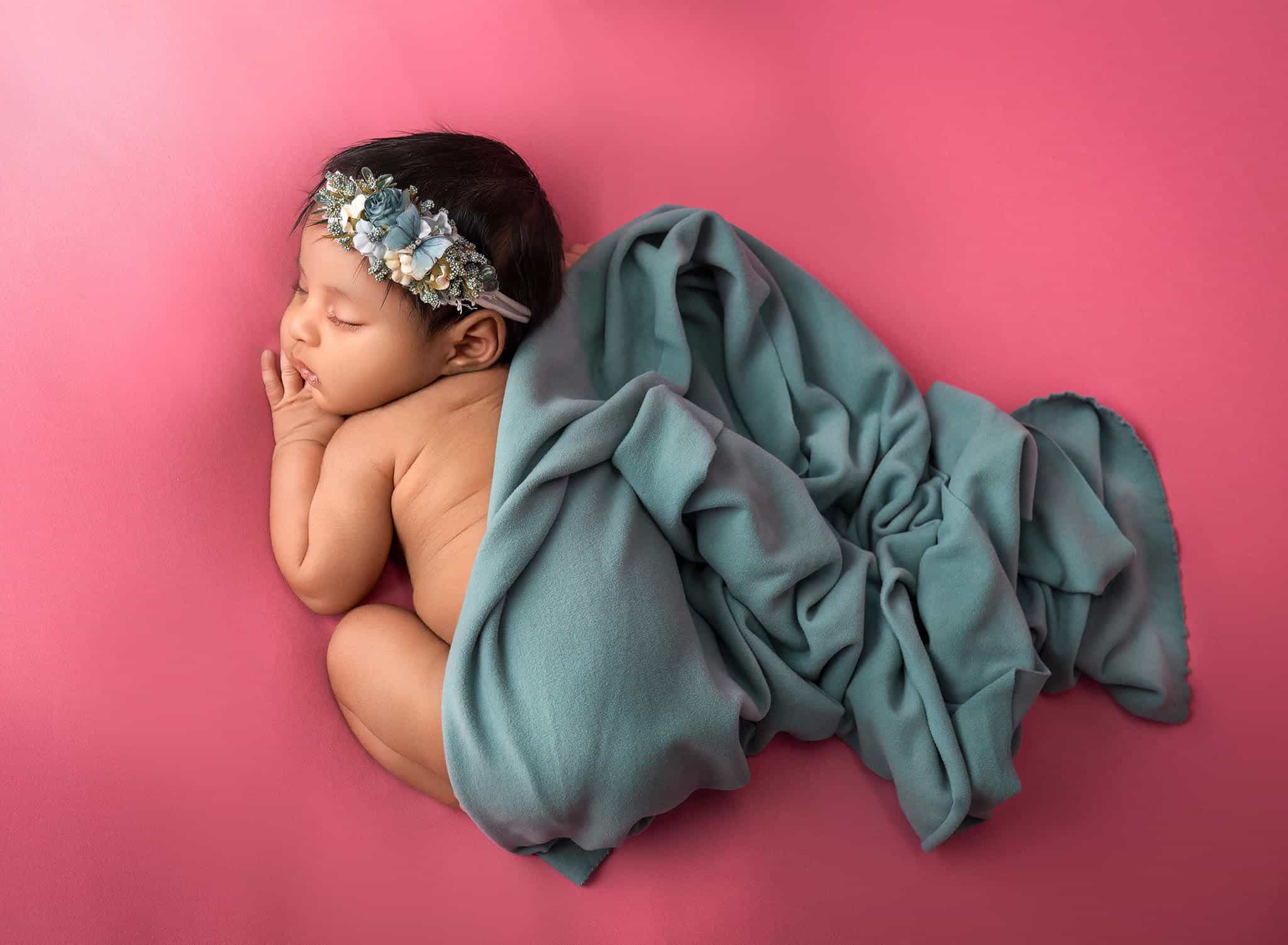 newborn baby asleep on coral backdrop with teal fabric draped across back