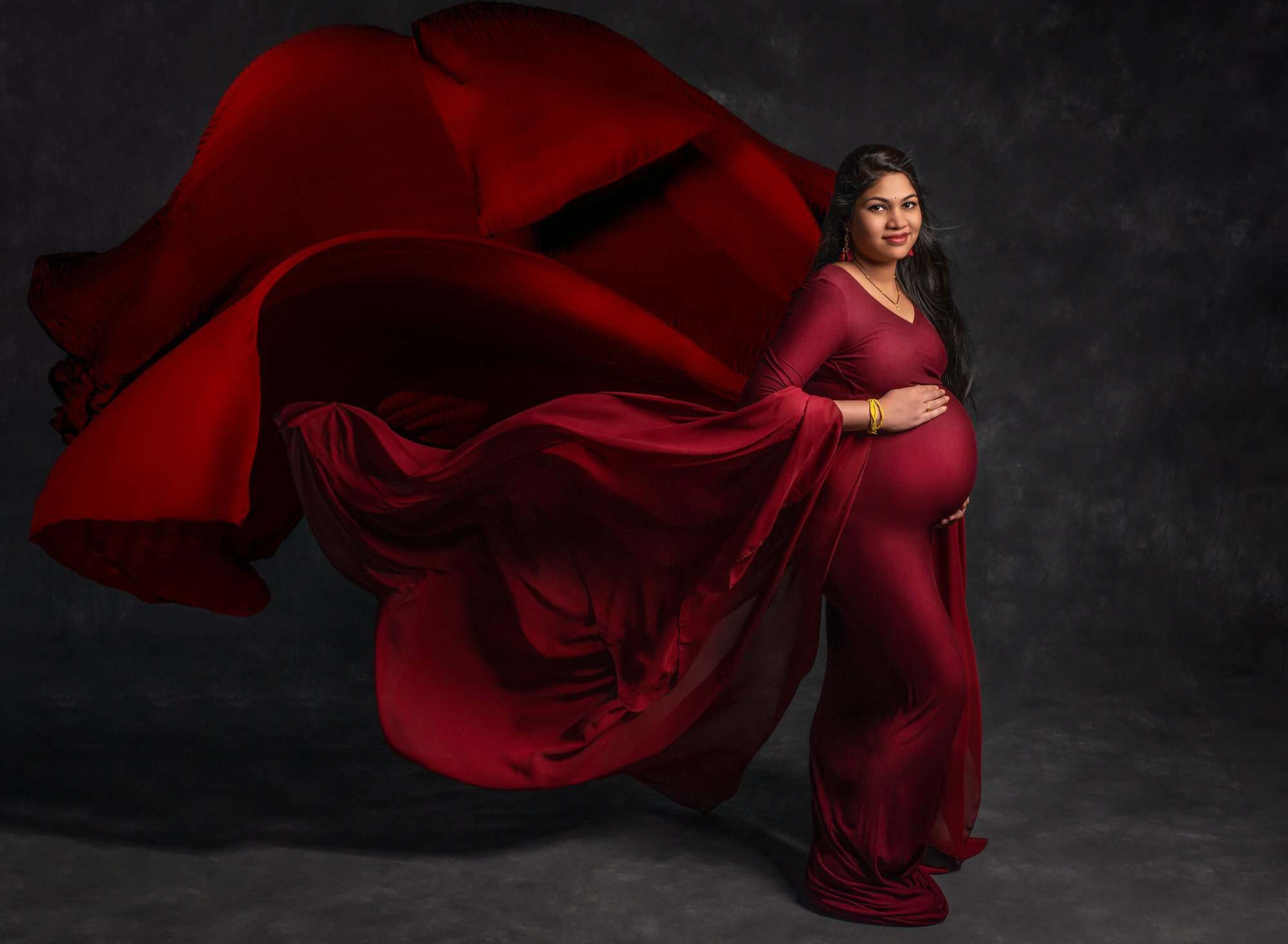 flowing cranberry maternity dress on dark gray backdrop