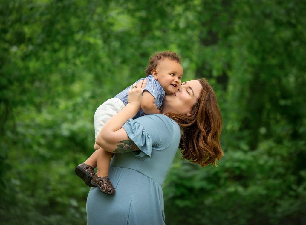 one year old boy being kissed on the cheek by his mother while outside