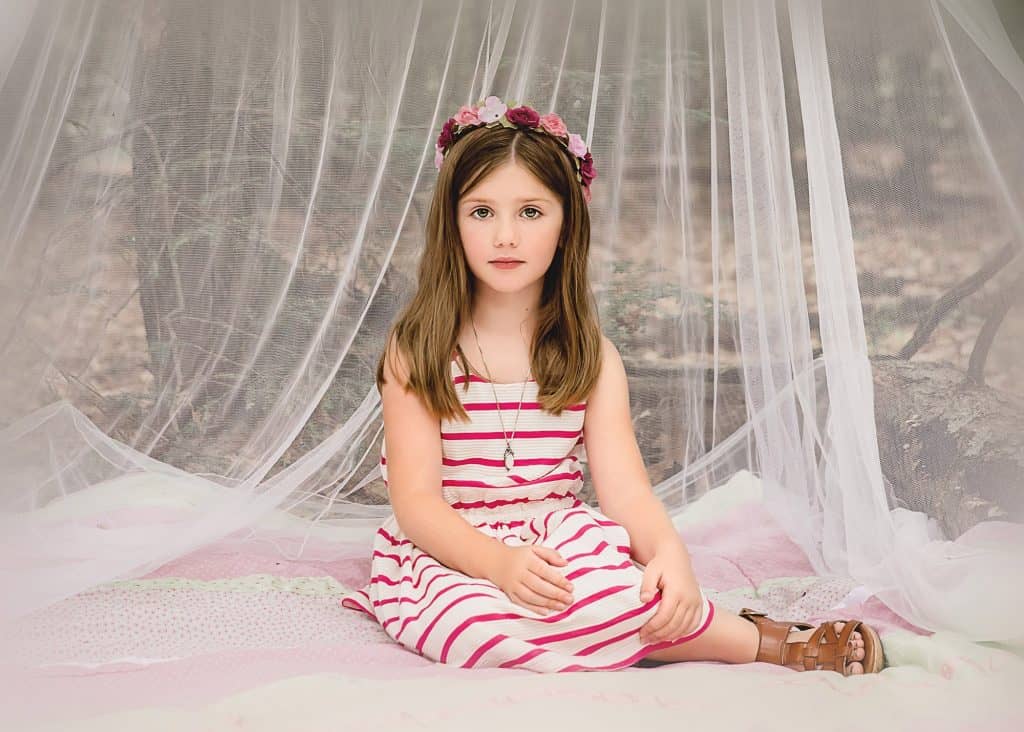 little girl sitting in a net tent out in the woods