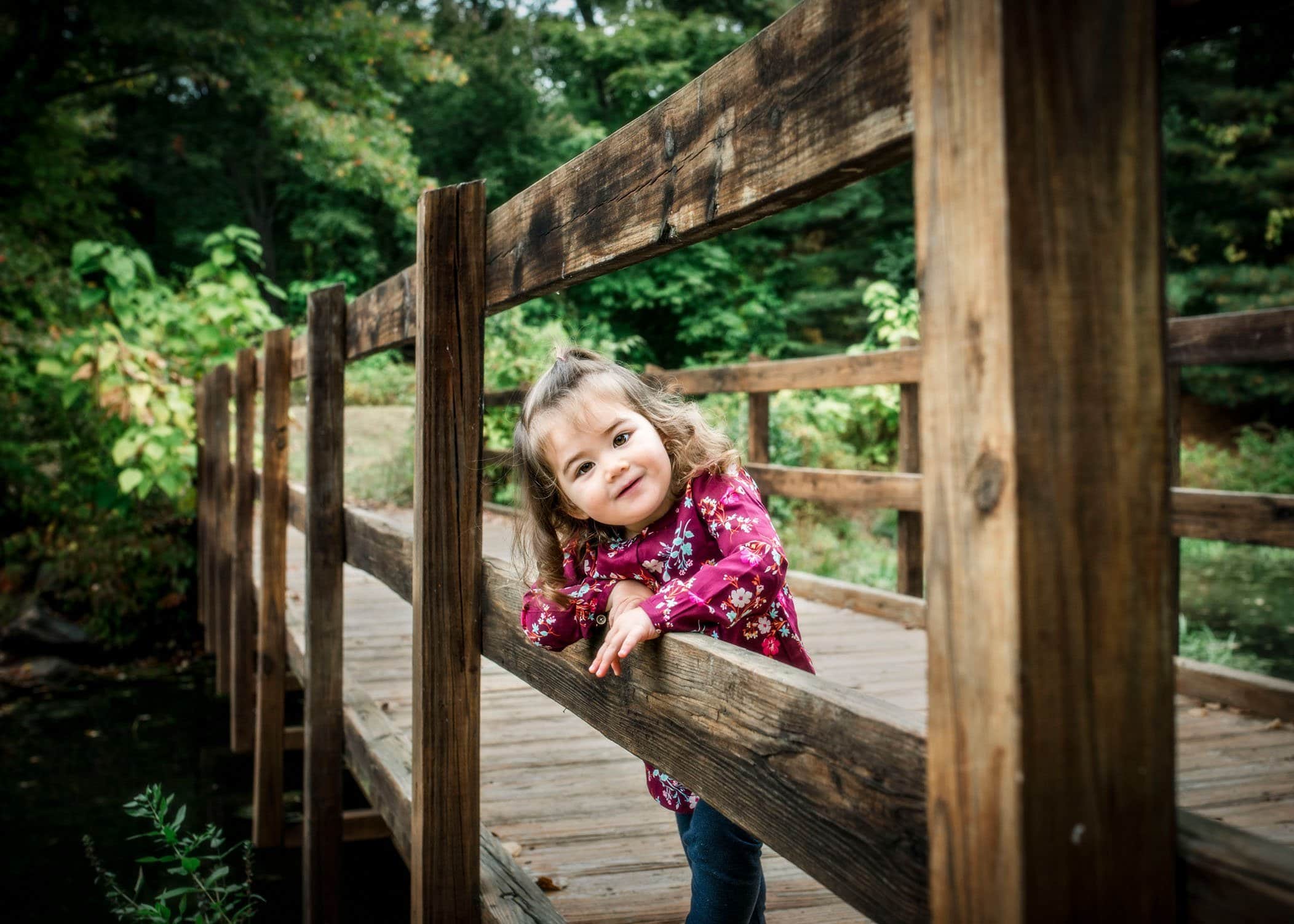 2 year old peaking through railings on a bridge