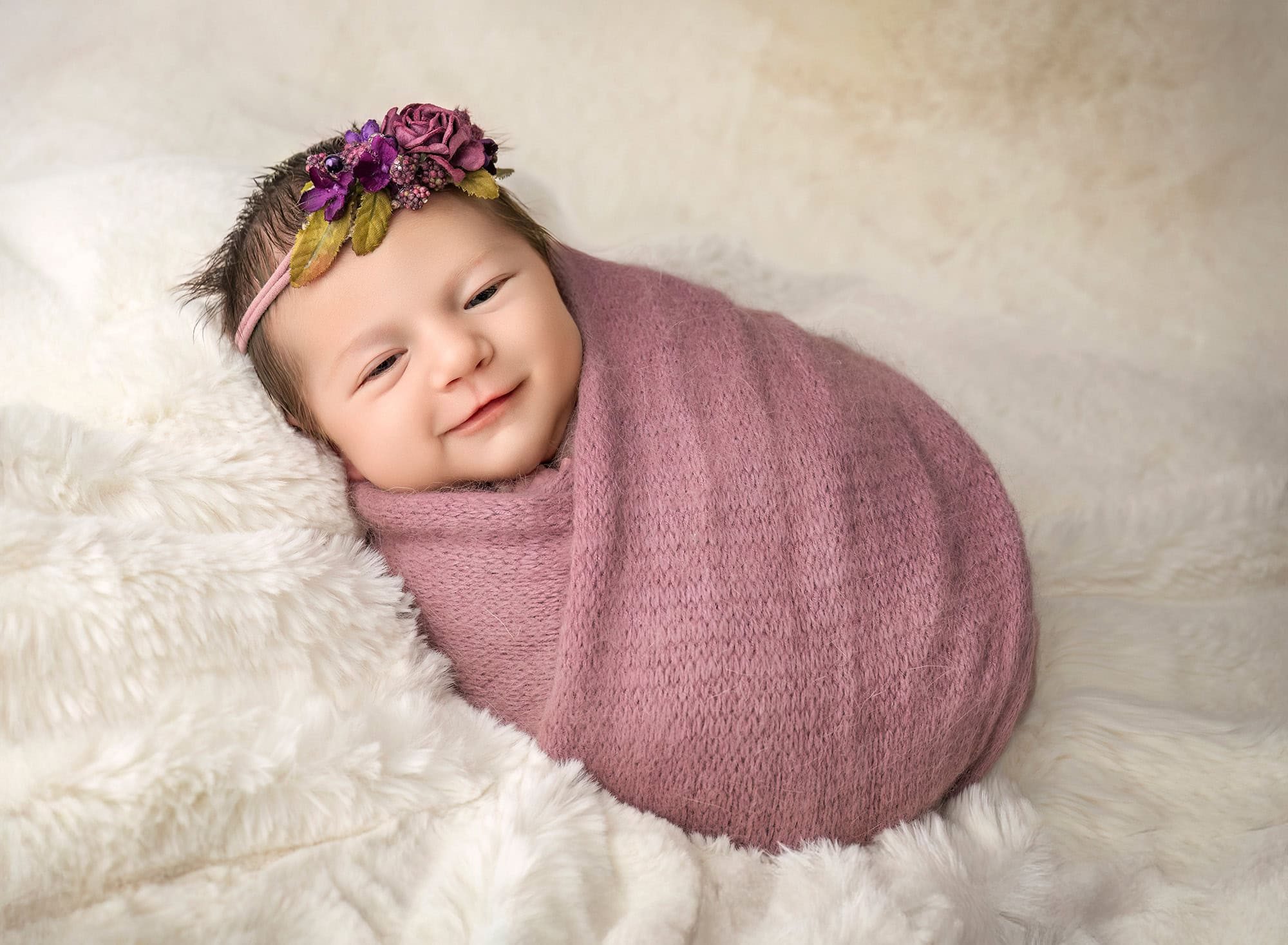 newborn photos with siblings — Violet swaddled in mauve, smiling on white fur