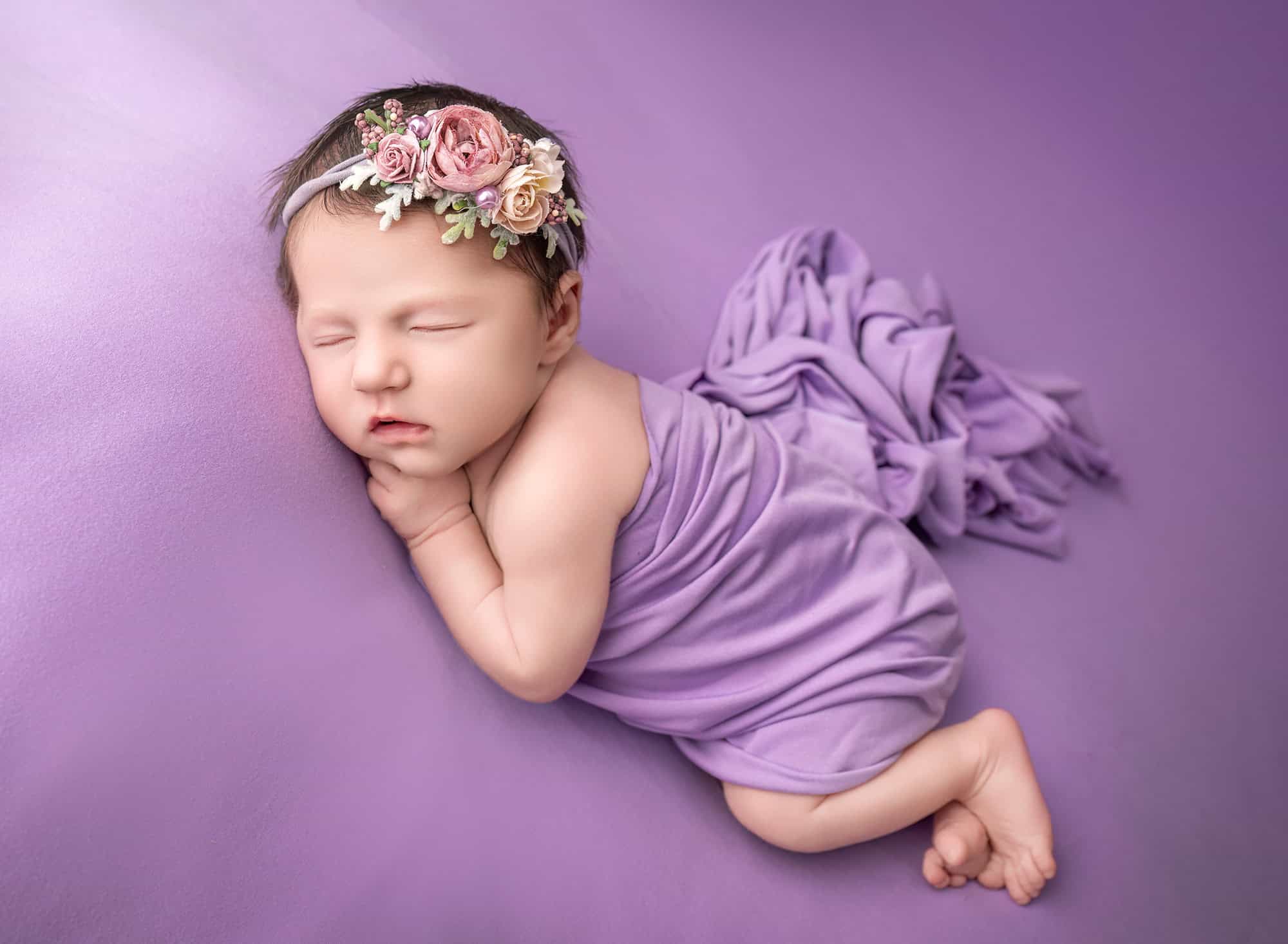 newborn photos with siblings — lavender wrap on purple backdrop, side-lying sleep