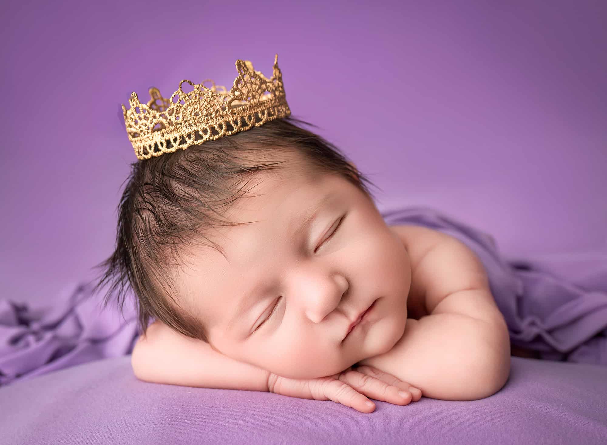 sleeping newborn with tiny gold crown on arms
