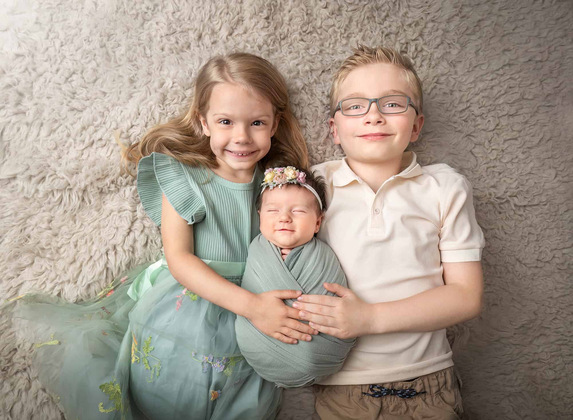 newborn photos with siblings — big sister and brother holding swaddled newborn
