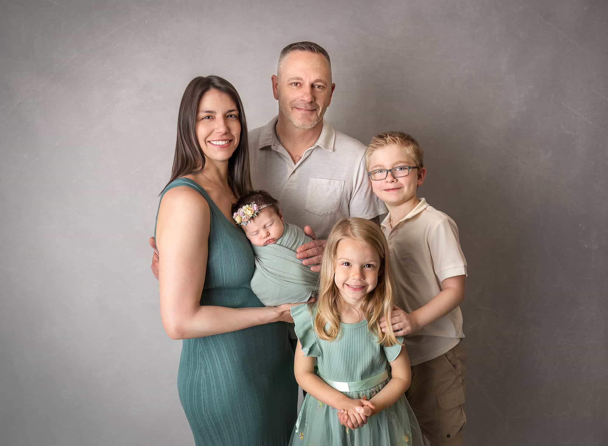 newborn photos with siblings — family studio portrait with newborn in parents’ arms