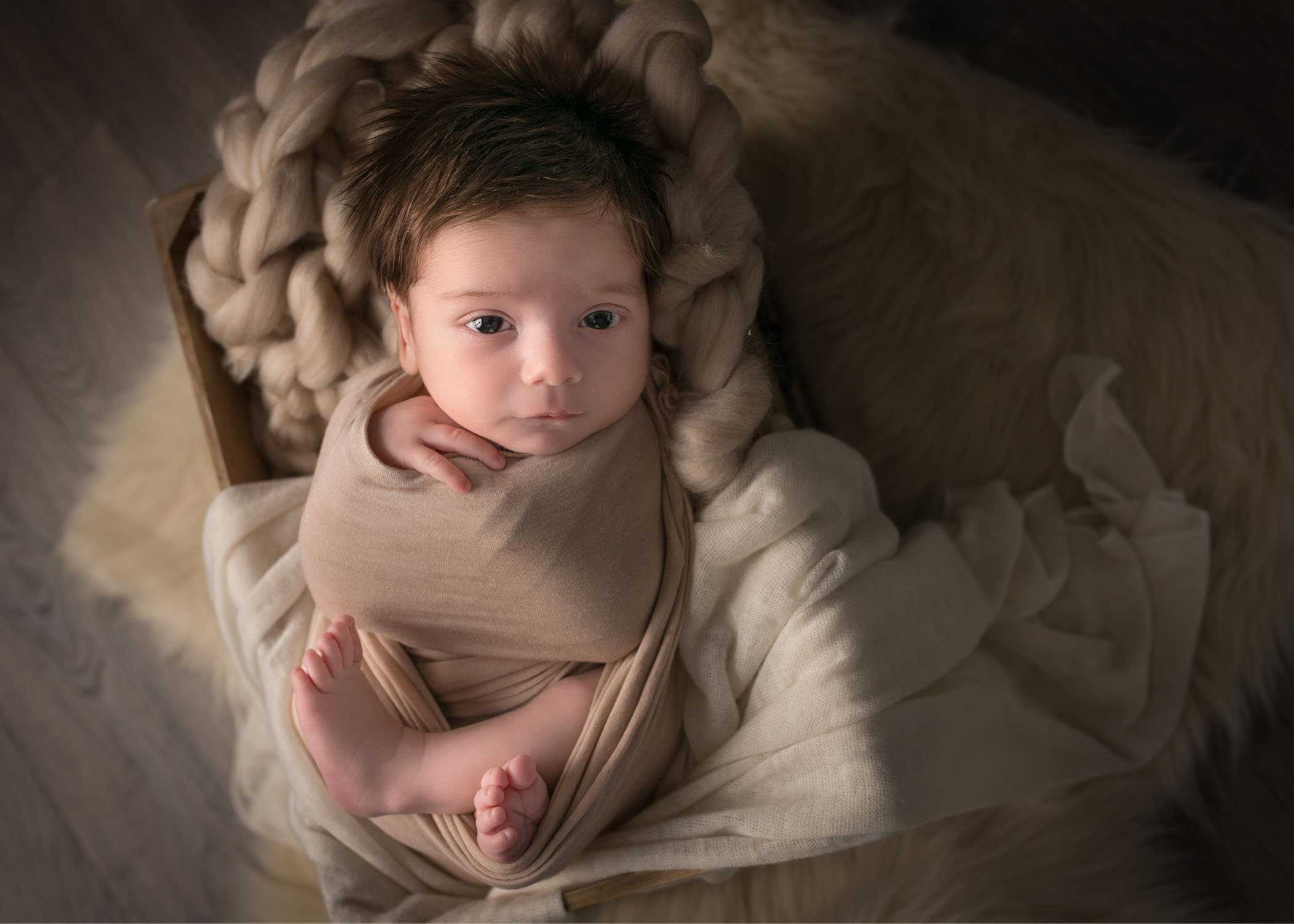newborn baby boy lying in wooden crate on knit layers peacefully looking at camera