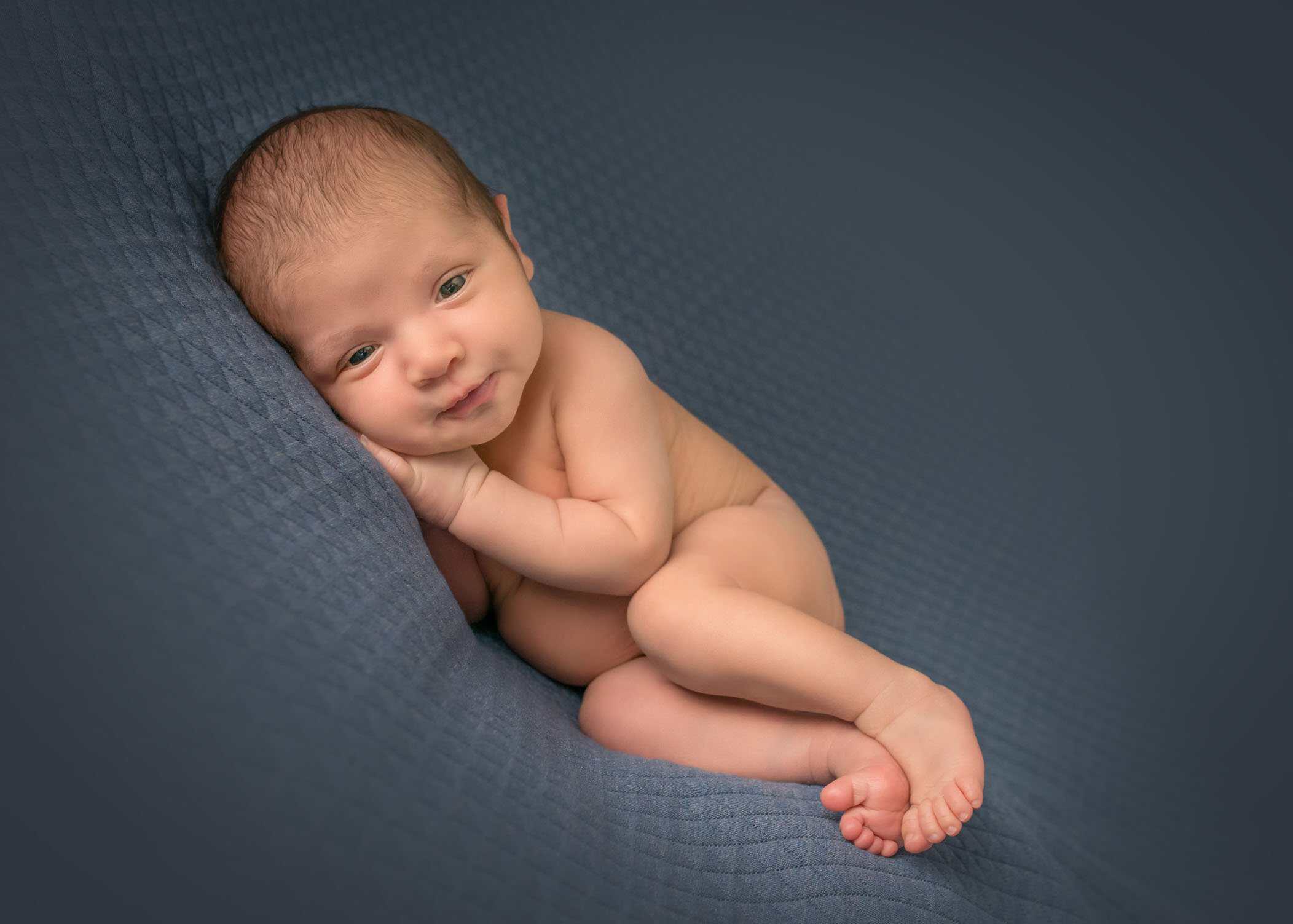 Newborn baby boy lying on his side on blue blanket looking at the camera