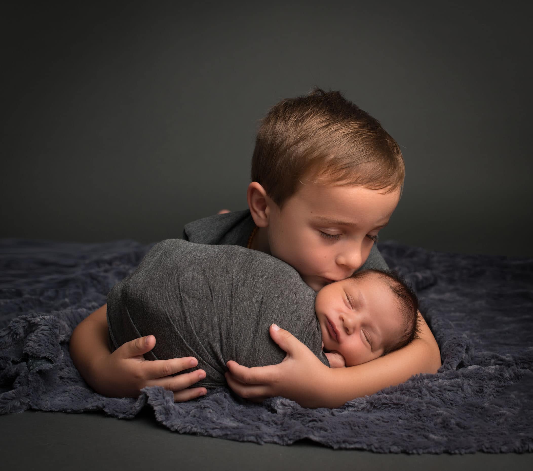 5 year old holding newborn in arms and giving him a kiss on the cheek