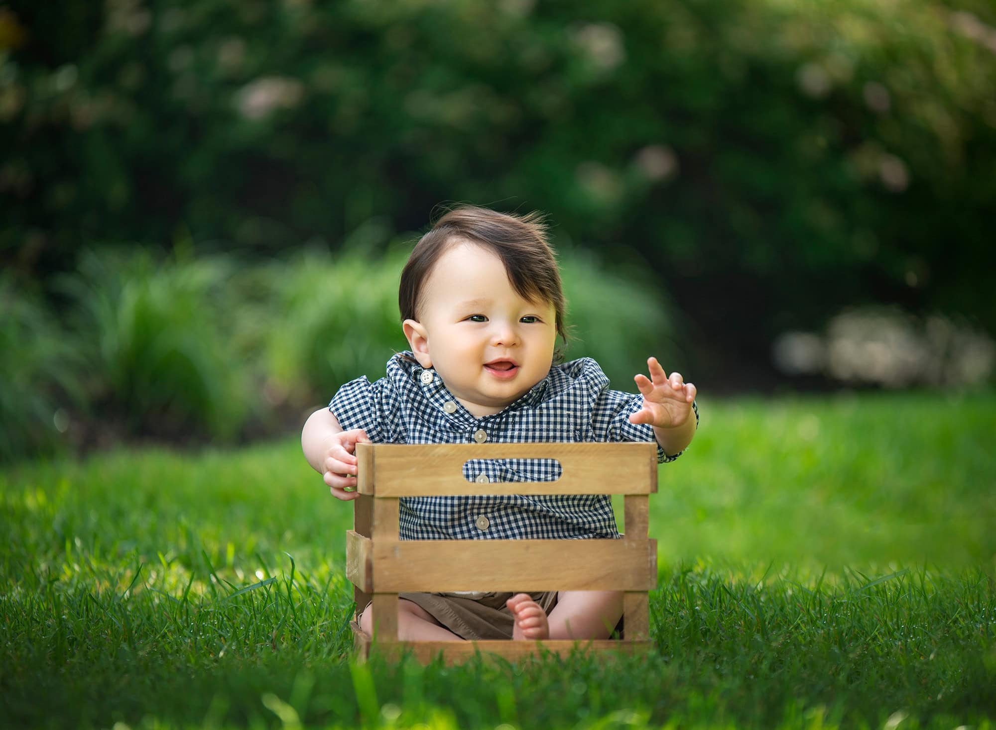 toddler in black and white checkered button up smiling while sitting in wooden crate