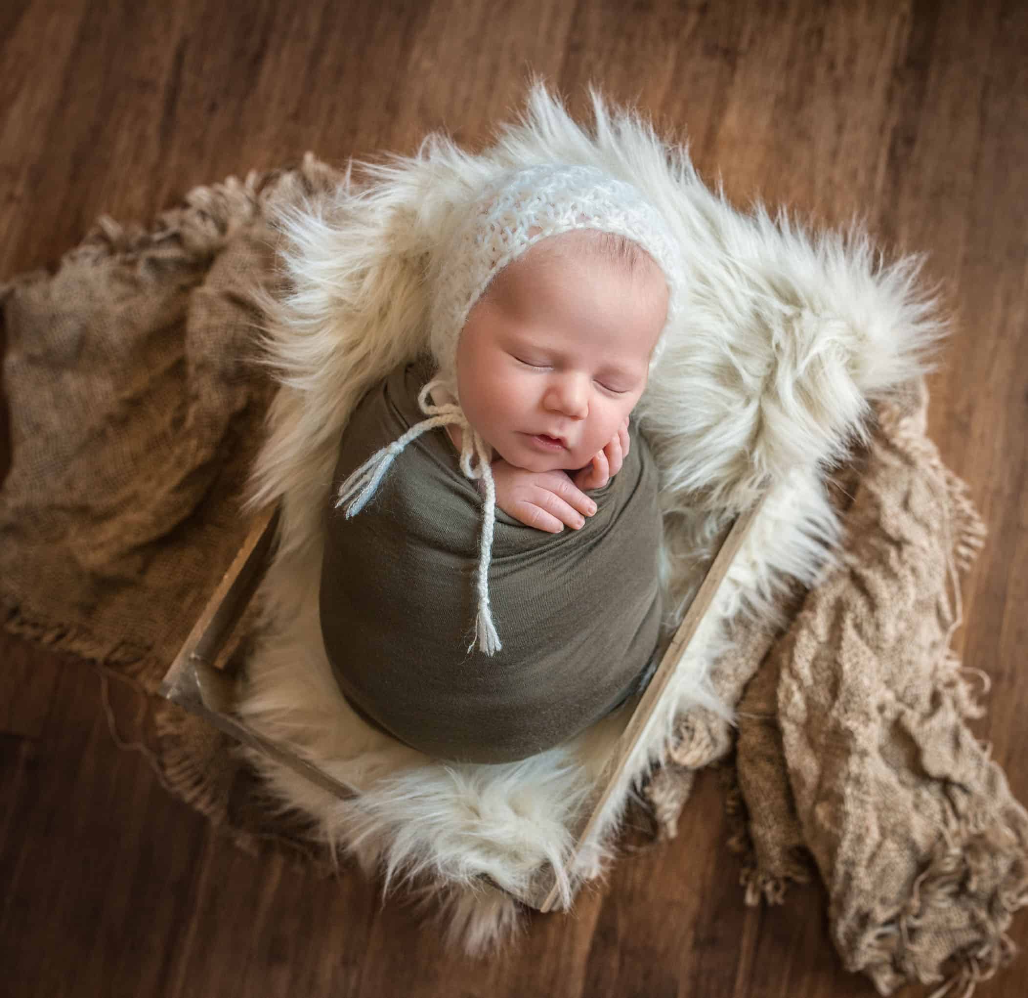 newborn baby boy lying in crate with fur