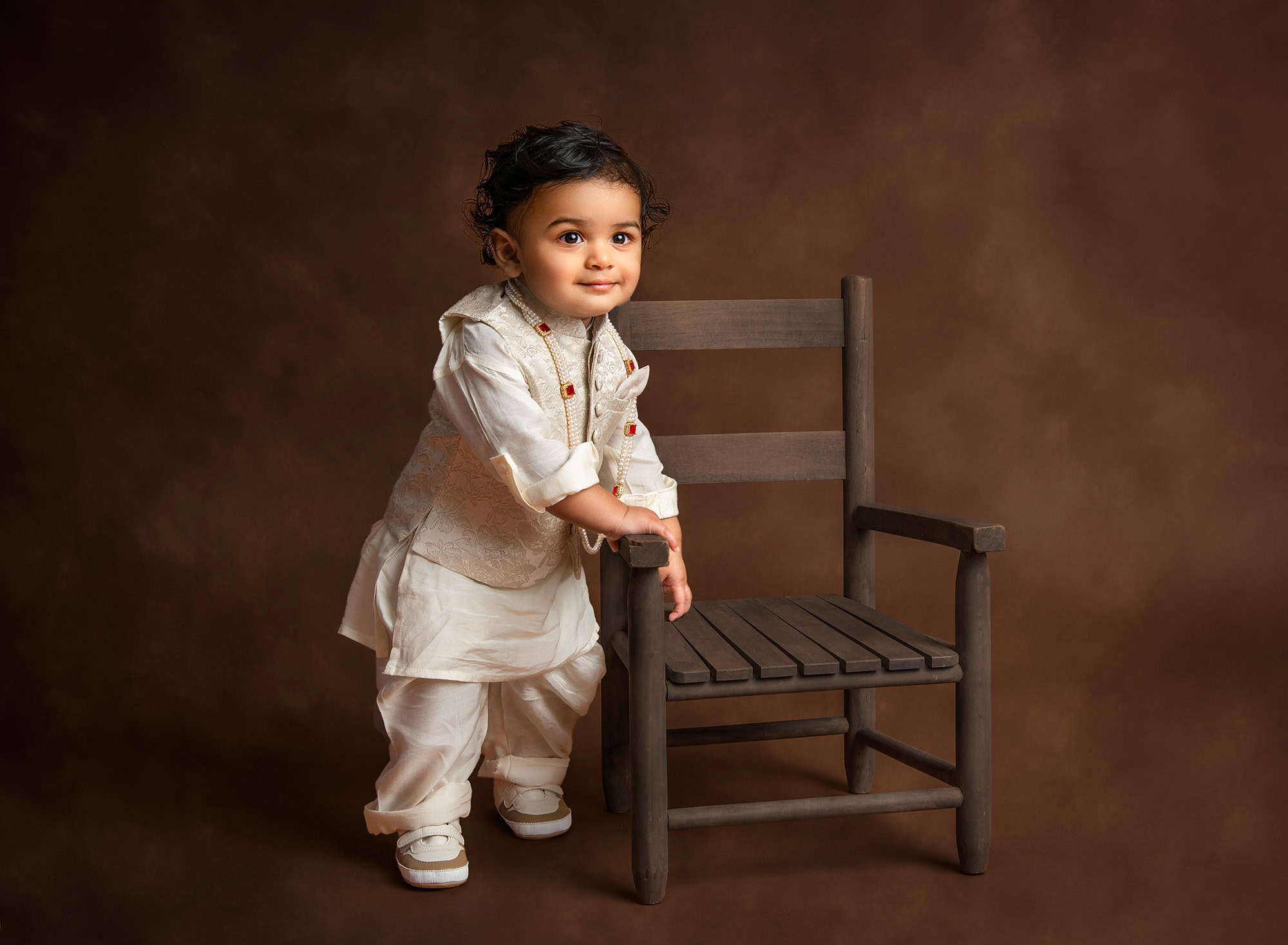 family professional pictures 1 year old indian boy dressed in traditional indian attire standing next to a toddler size chair
